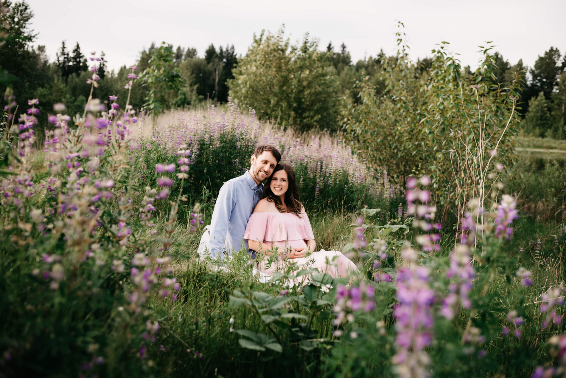 Couple sitting in a field of lupine wildflowers during a maternity photo session in Redmond WA