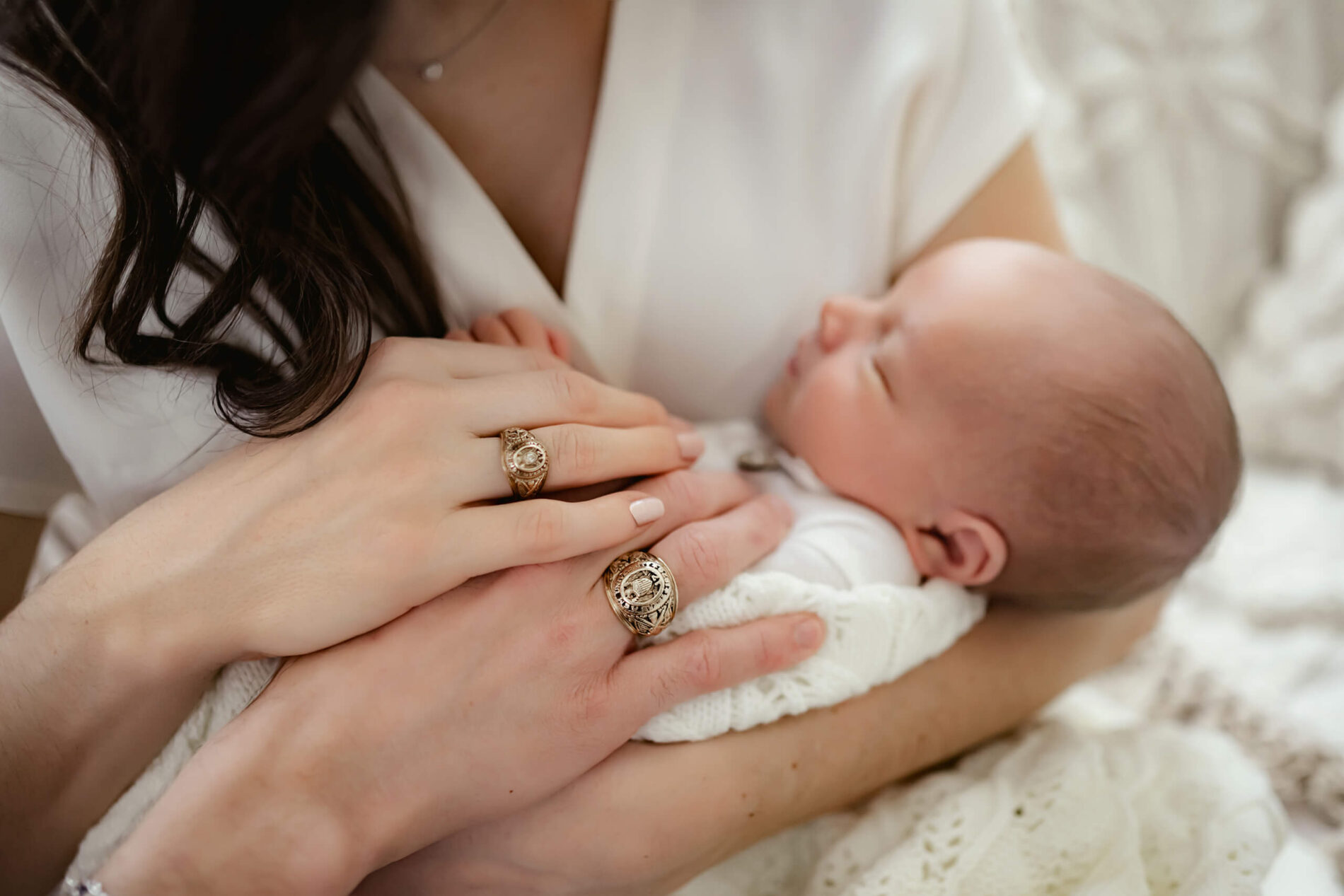 Mom cuddling with her newborn son during a photoshoot. Dad's hand is also present in the photo, lying gently on the baby.