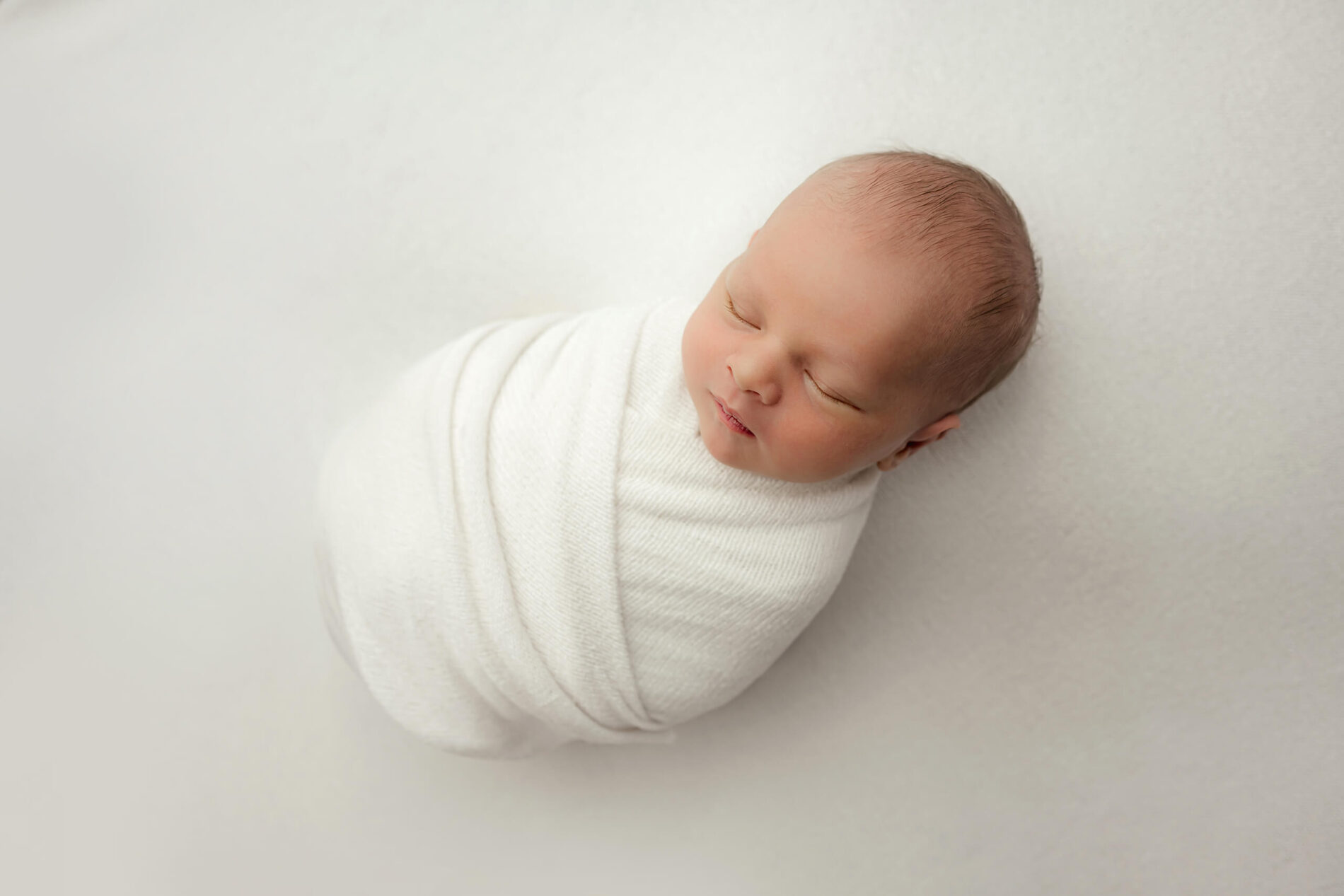 Elegant and timeless newborn photo of a boy, wrapped in white blanket on white background
