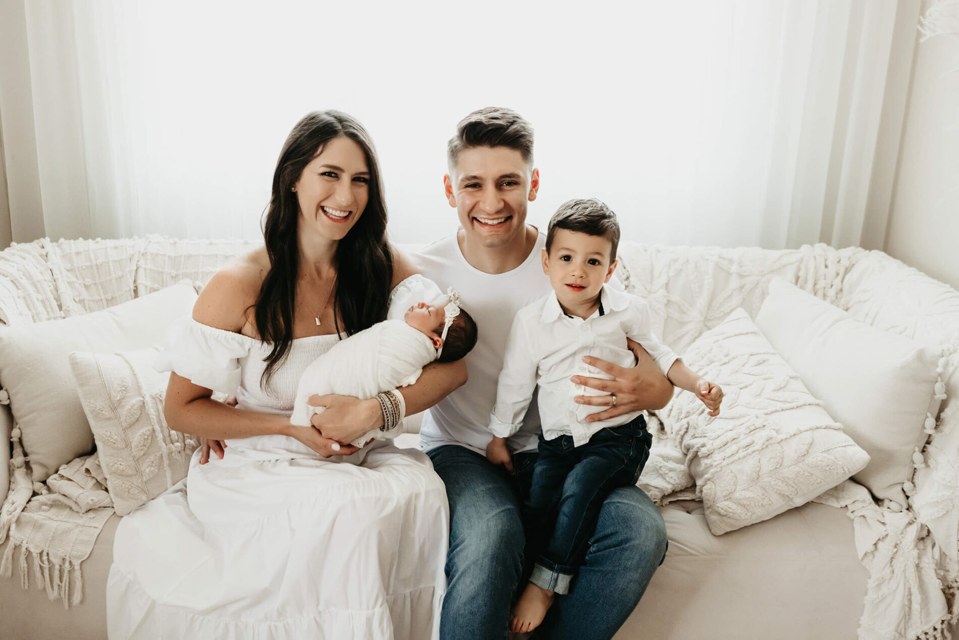 Family newborn photography in a Seattle studio. Mom and dad sitting on a couch with toddler son and newborn daughter.