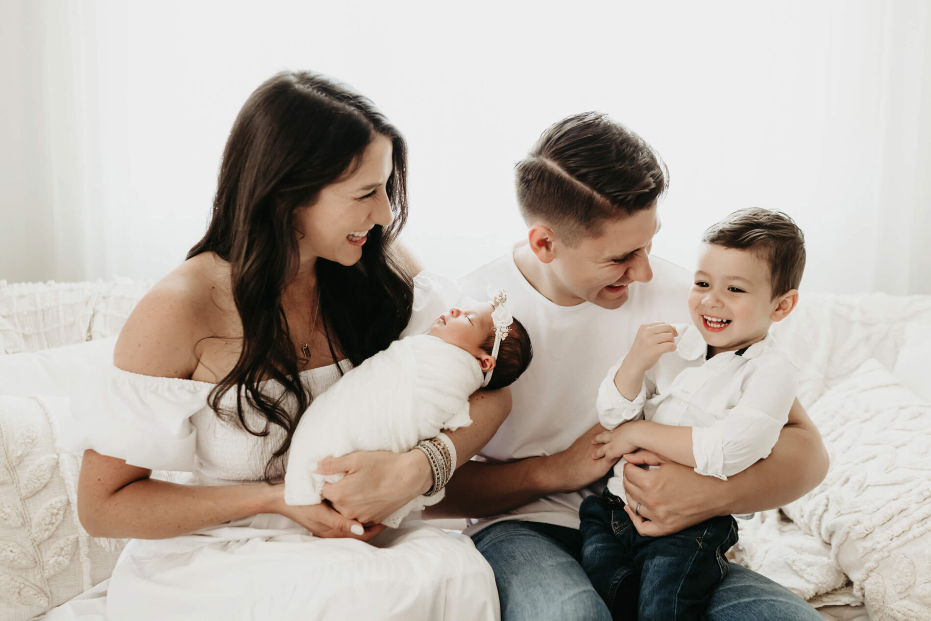 Natural newborn photography with family. Mom and dad having a fun time with their sleeping newborn daughter and toddler son.