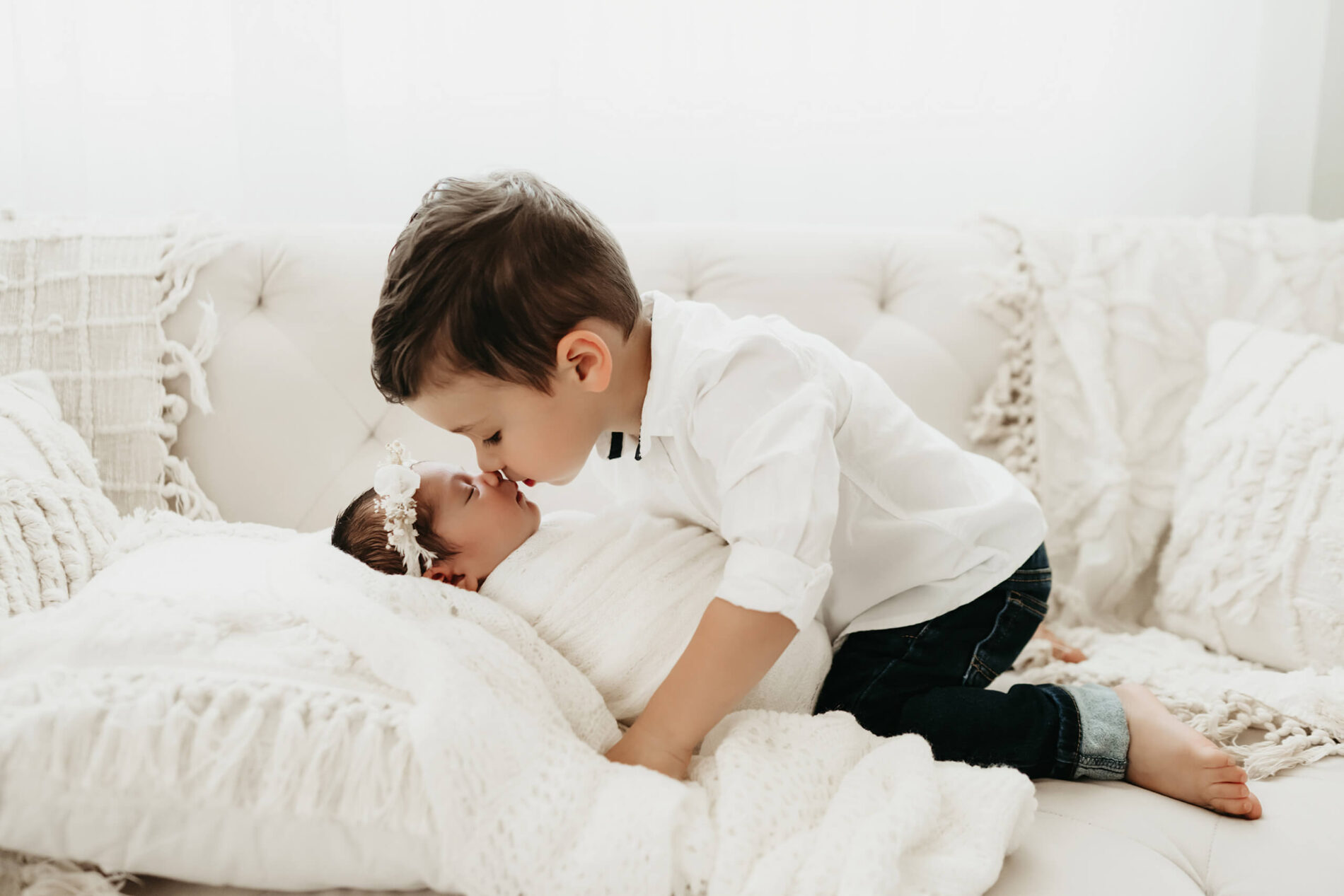 Newborn photography with a toddler and newborn girl. Older brother touching noses with baby sister in a Seattle studio.
