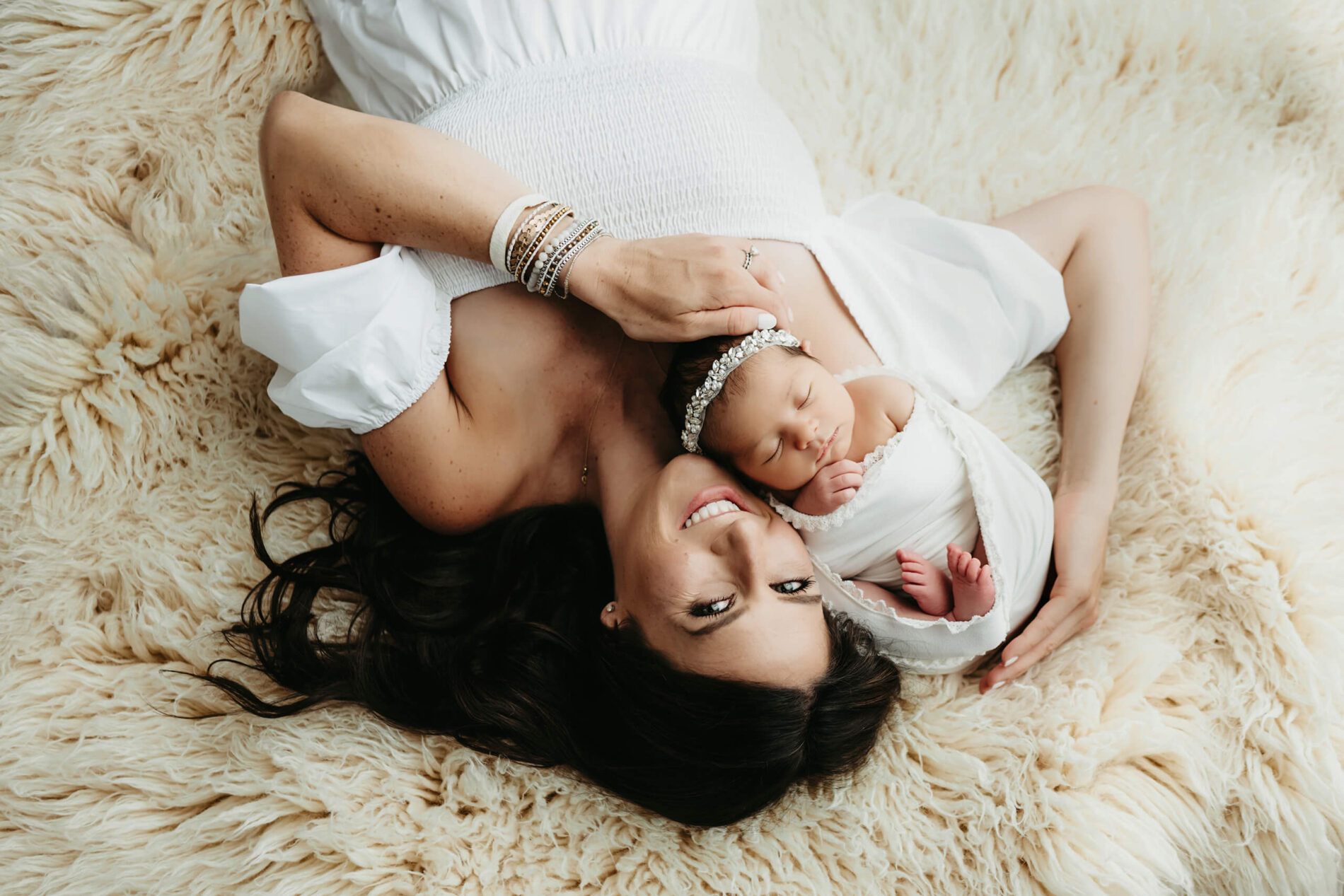Unique newborn pose of mom and baby. Smiling mom lying on the white rug on the floor with her baby posed next to her in a Seattle studio.
