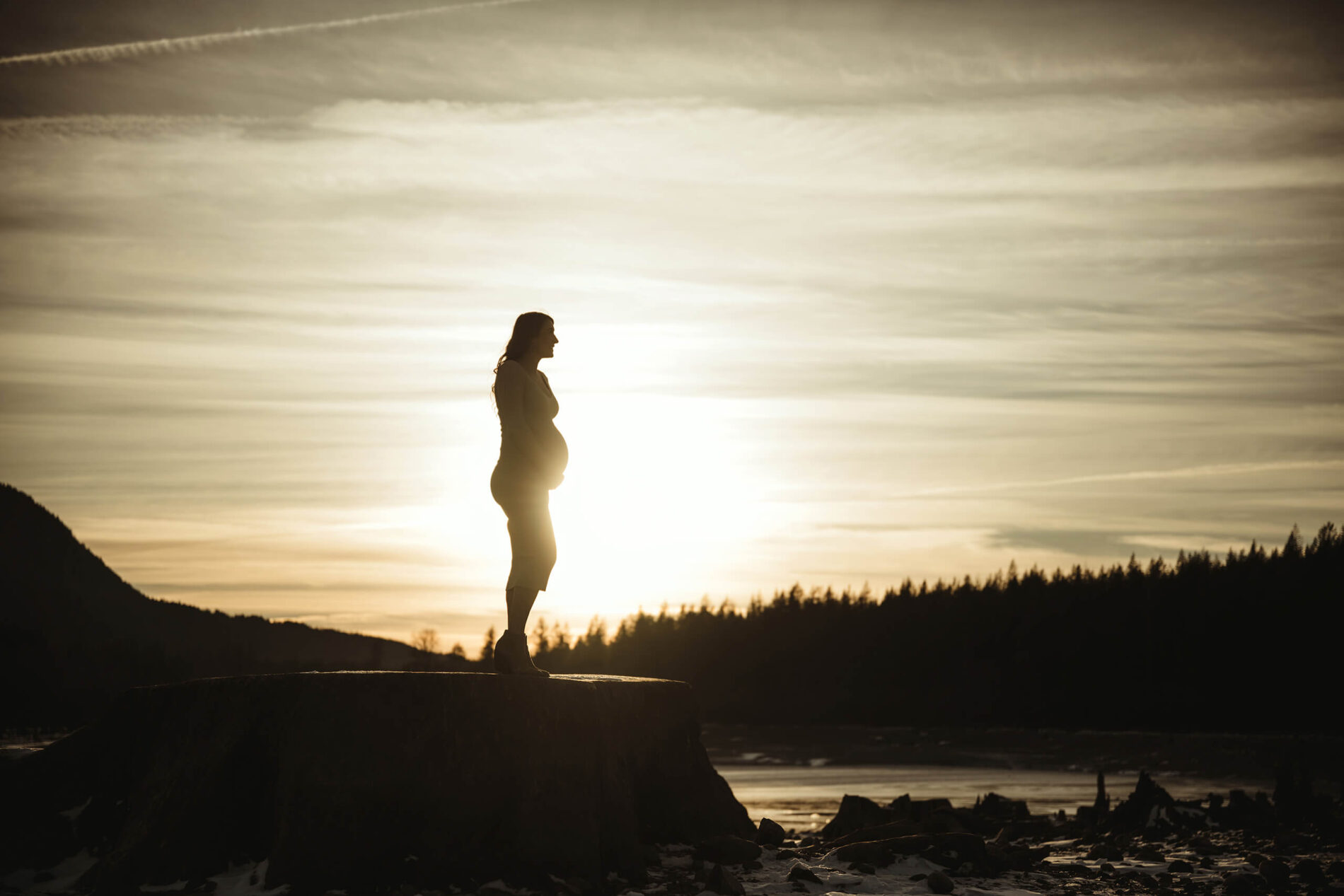 A gorgeous silhouette maternity photo in Seattle of a pregnant woman during sunset with frozen lake and mountains in the background