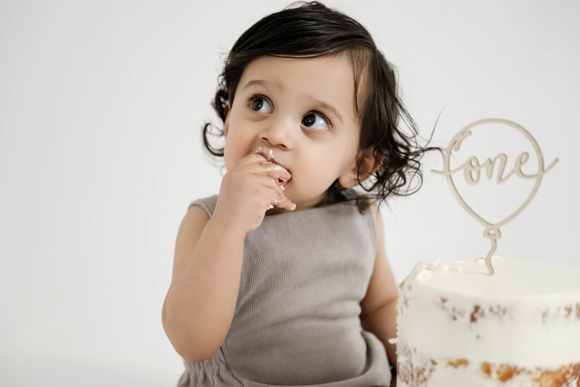 A close-up on a boy's face with his hand covered in cake in his mouth during cake smash photo session