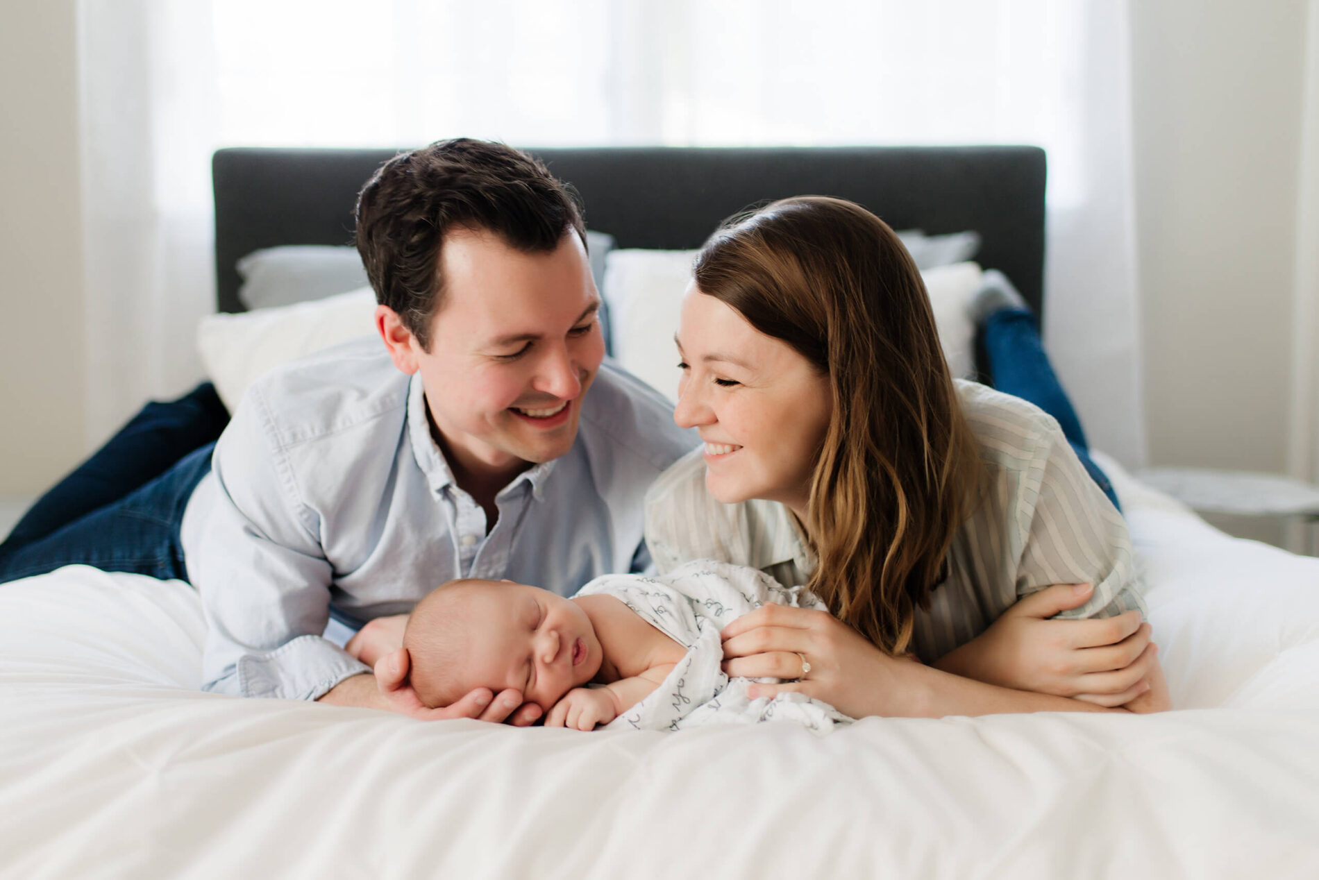 Newborn in home photoshoot, mom and dad lying with their infant on the bed