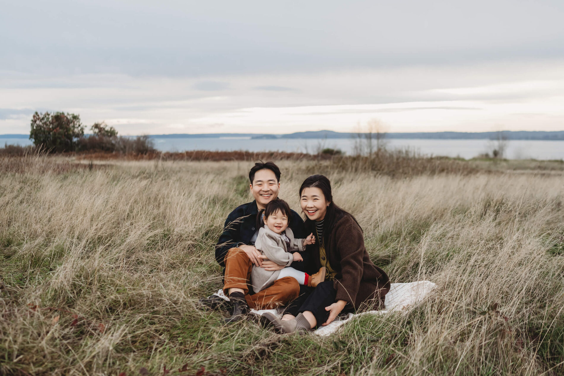 Family of three being posed in a field during family photoshoot at Seattle Discovery Park
