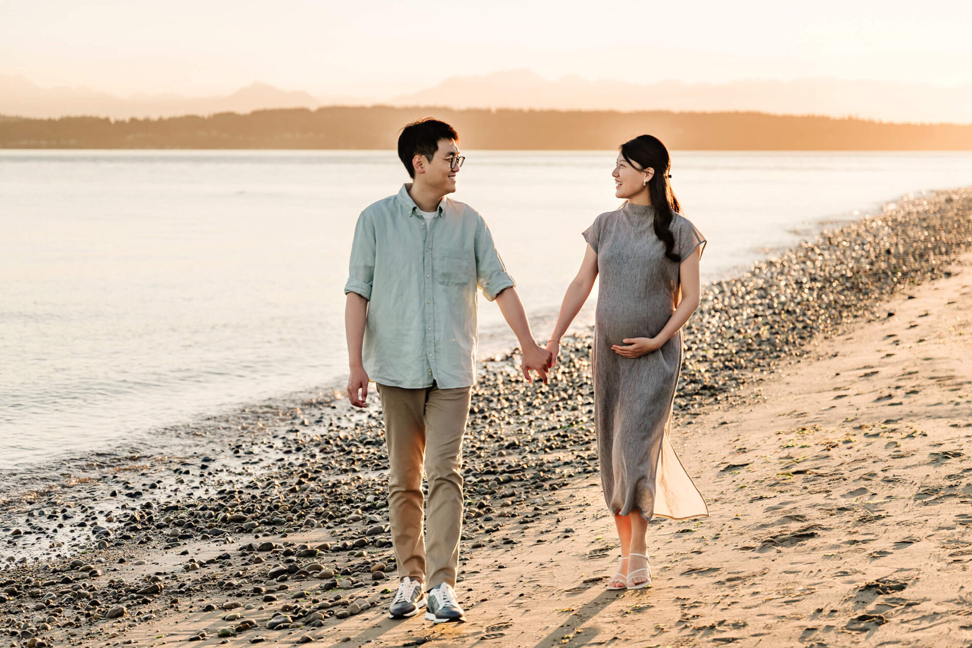 Young couple holding hands on a beach during pregnancy photoshoot in Bellevue area