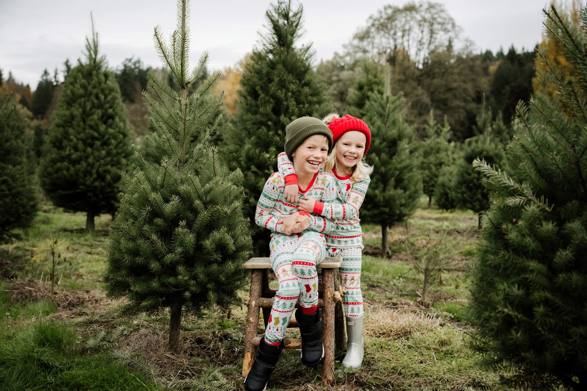 Two siblings in pajamas during a photoshoot at a Christmas tree farm