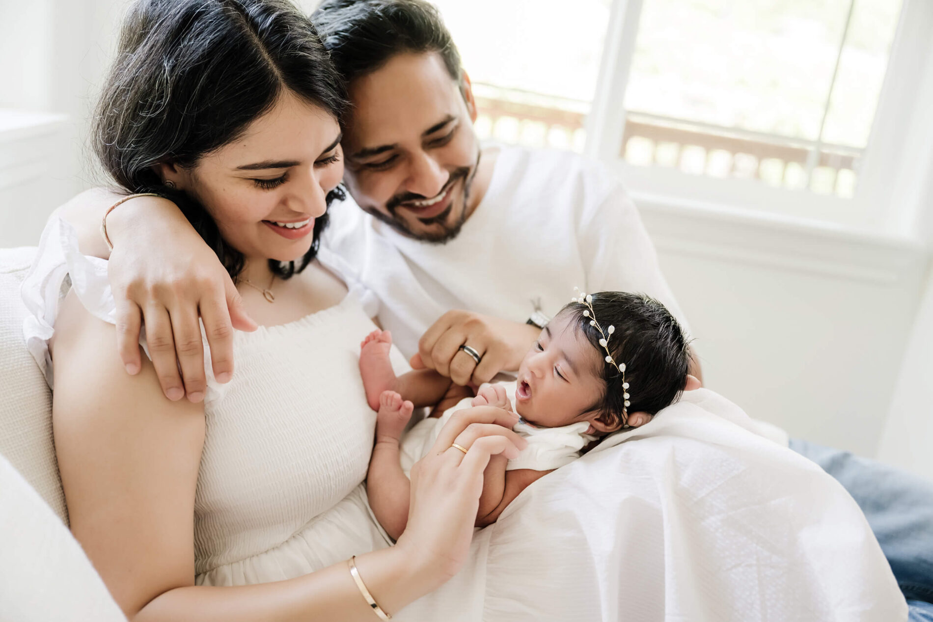 Parents on a couch, cuddling with their newborn daughter during in-home photoshoot