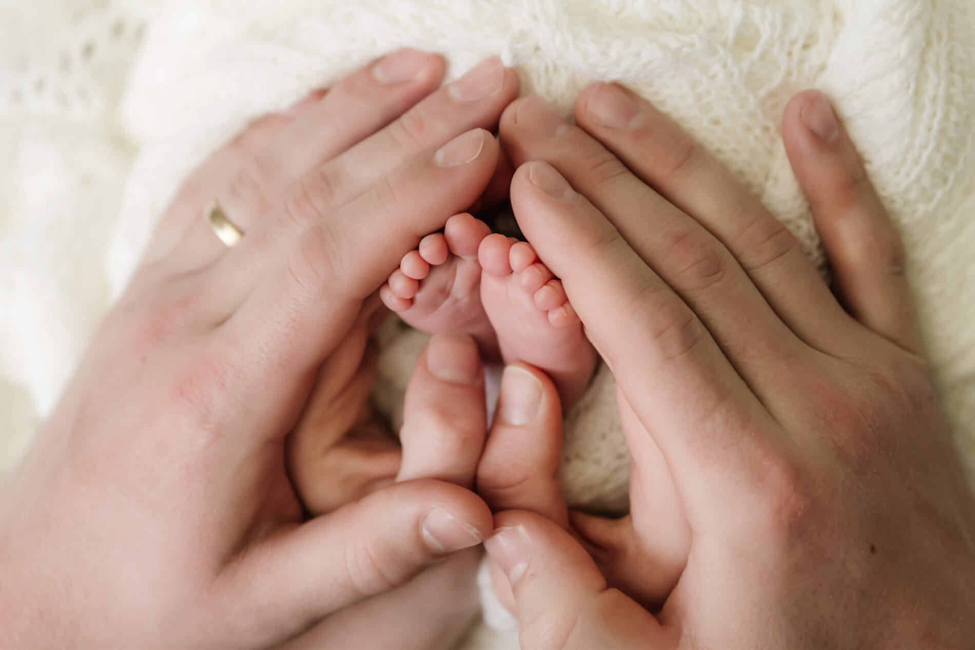A close-up portrait of parent's hands around baby's feet