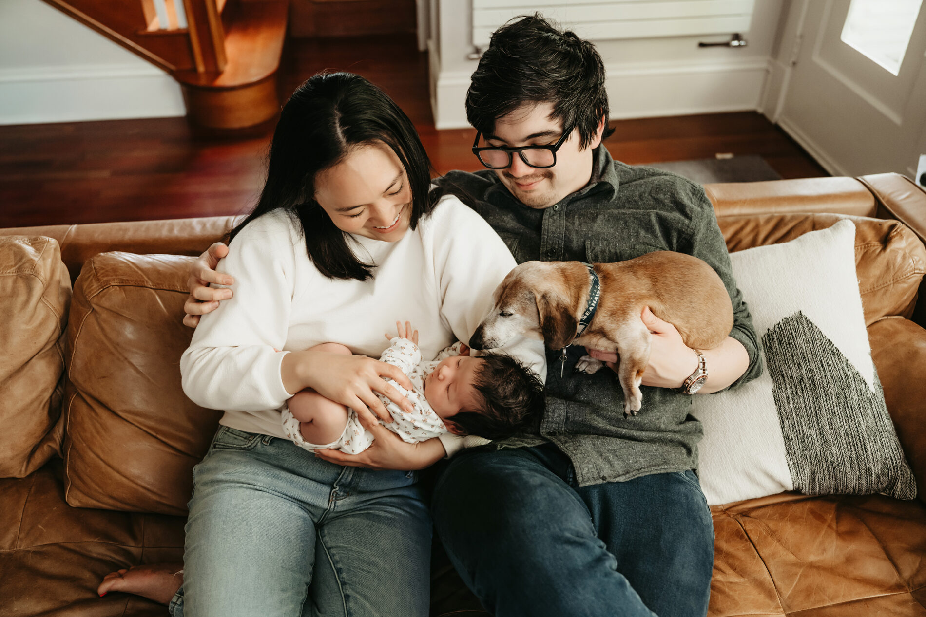 Parents cuddling with their newborn son and dog during in-home newborn photoshoot