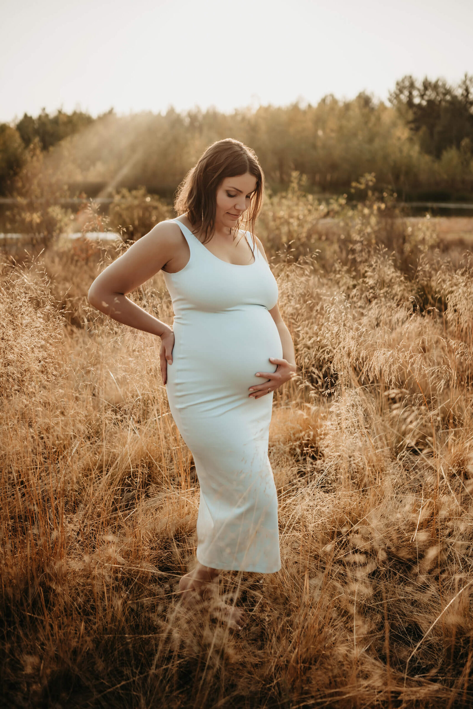 Maternity photographer posing a pregnant woman in a field with tall grass in Seattle area