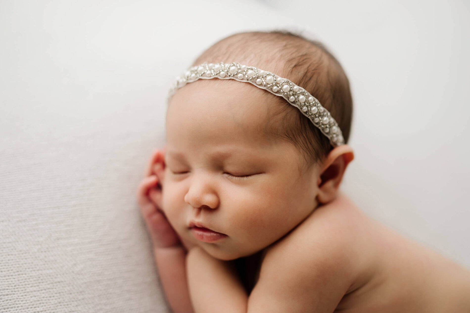 Side-lying infant, bare skin against textured knit fabric—simple pose that shows newborn’s gentle curve.