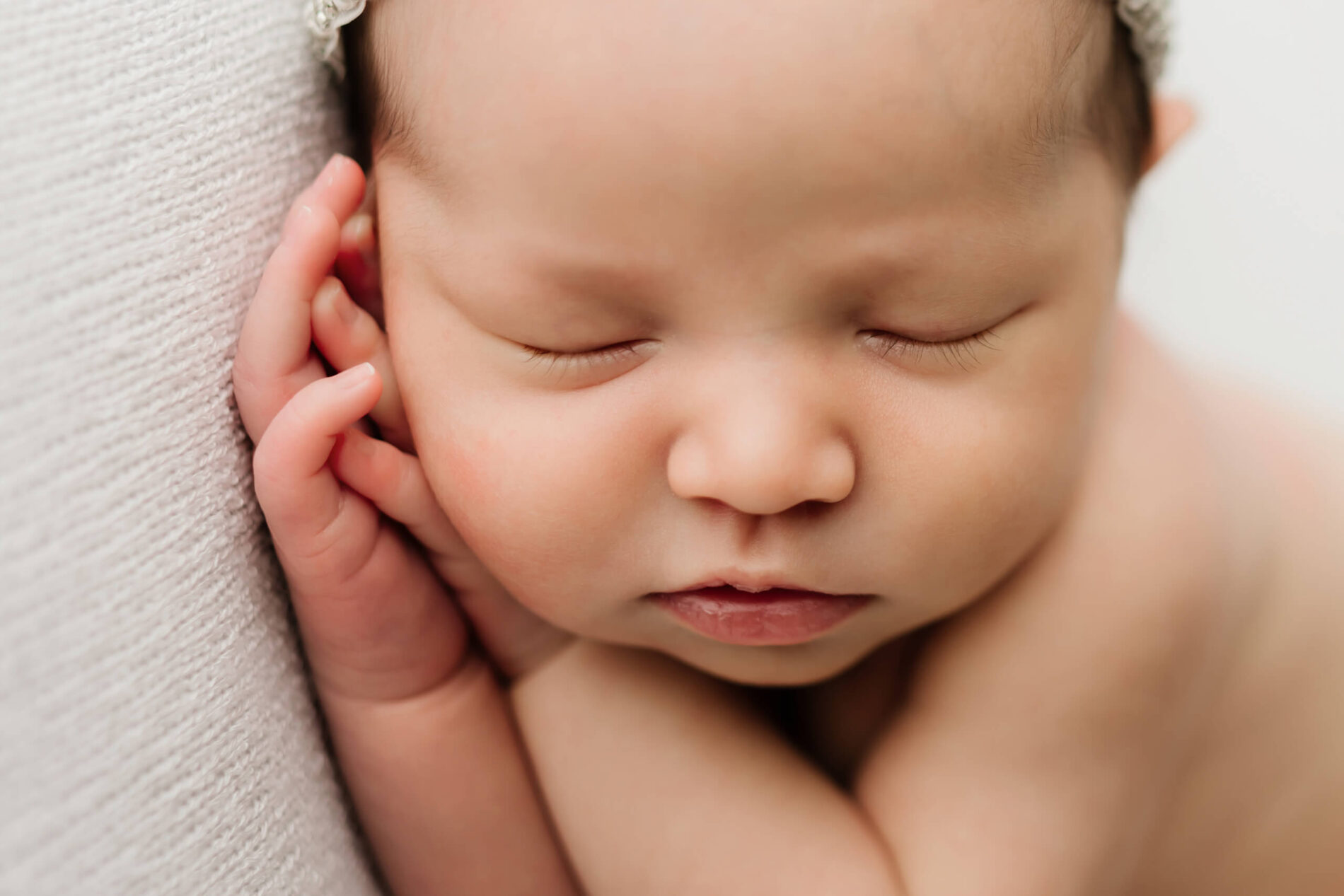 Close-up of sleeping newborn girl resting on cream blanket, soft studio light