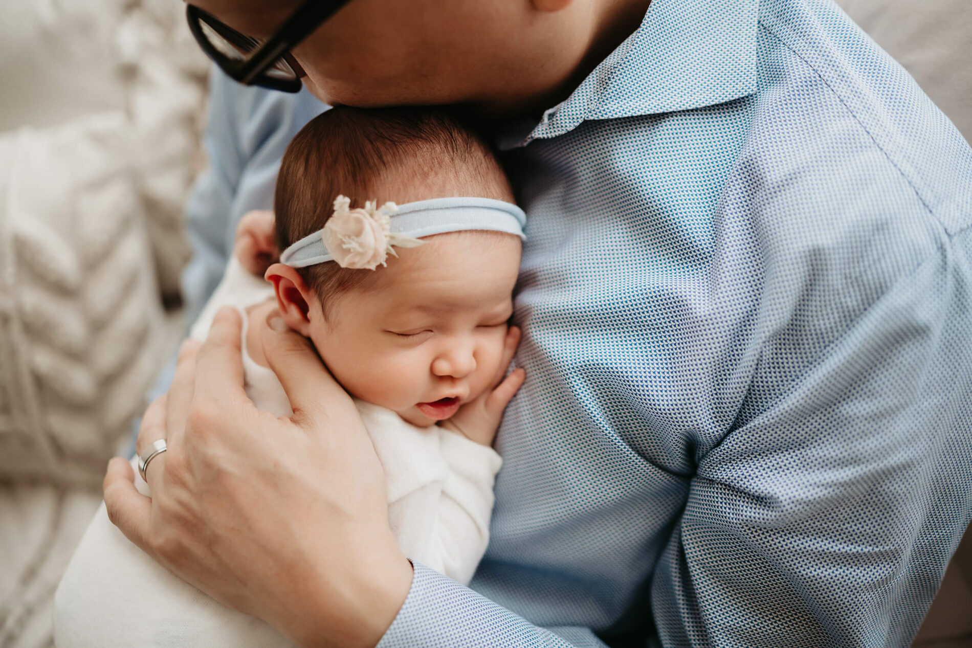 Close cuddle: infant sleeps on dad’s chest, pastel headband and soft studio light adding a gentle glow.