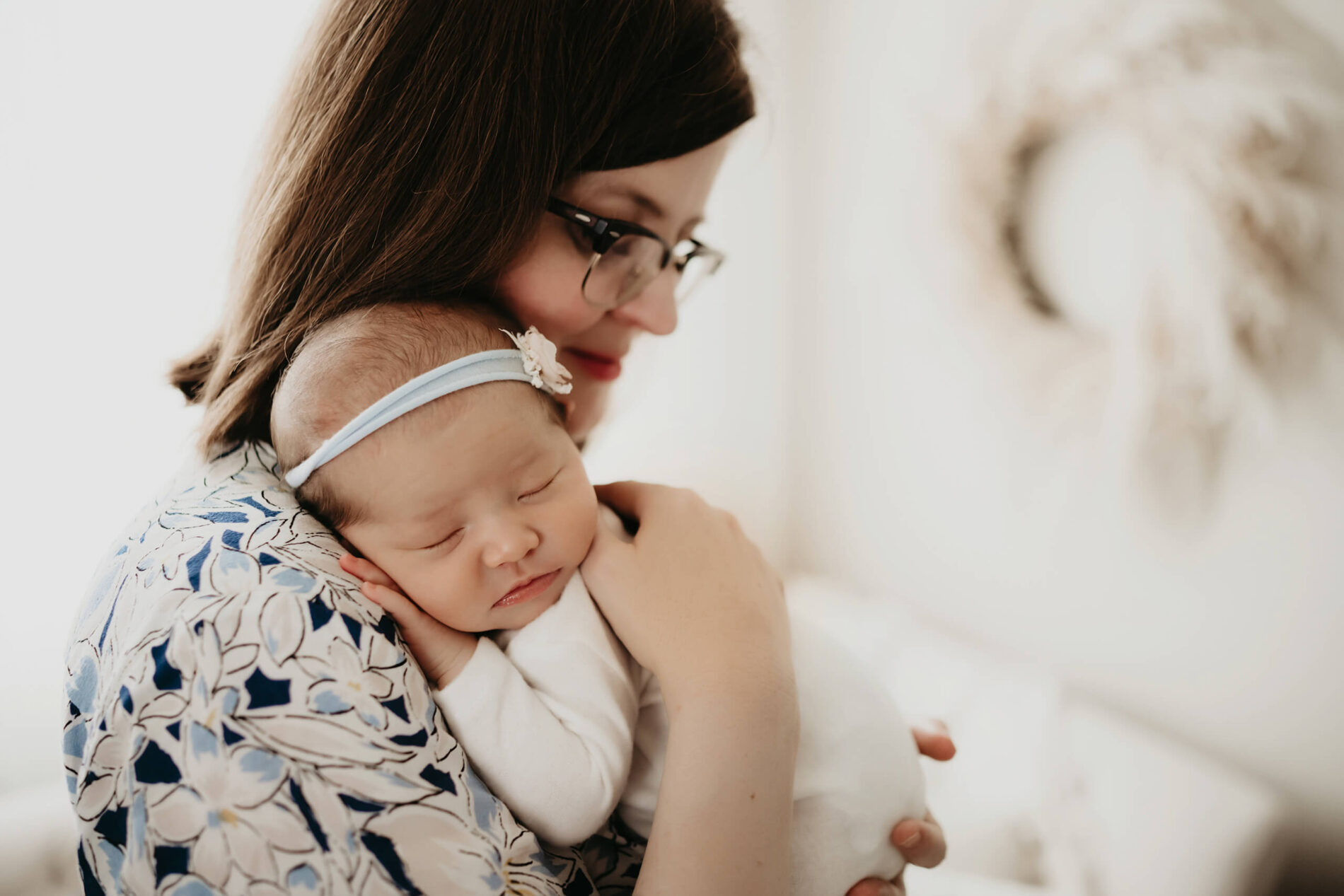 Baby girl dozing against mom’s shoulder; mom’s patterned dress adds a pop of soft blue floral.