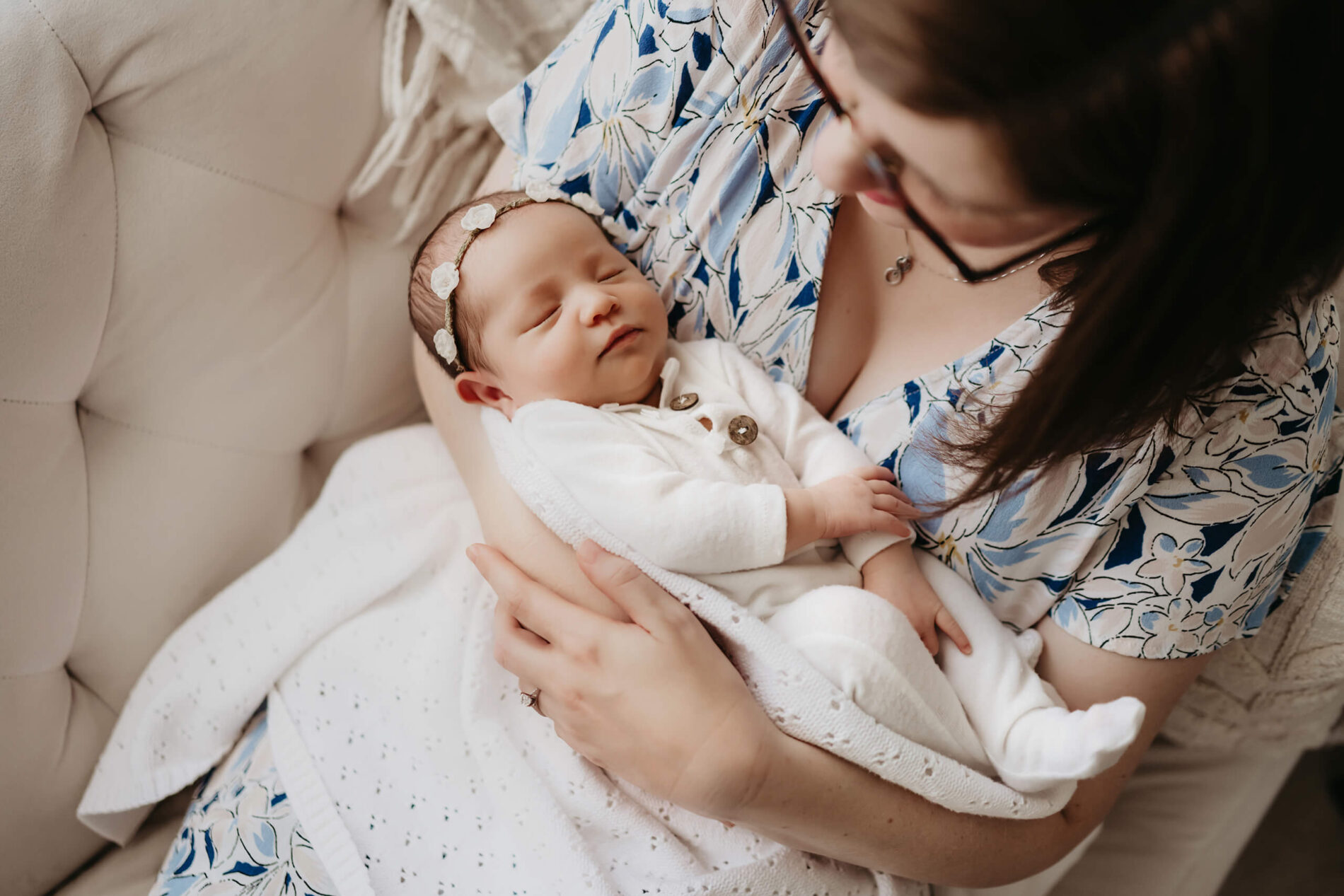 Couch cuddle: mom in floral dress holds sleeping baby wrapped in white
