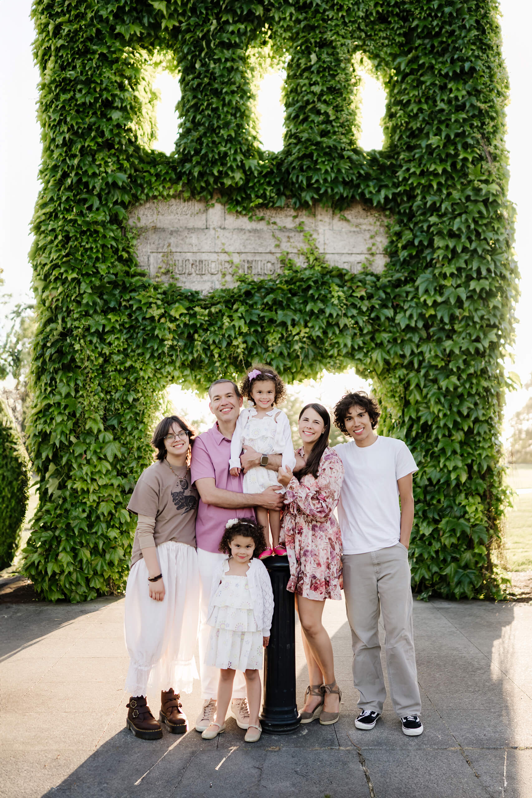 Family of six poses together beneath a towering ivy-covered stone arch at Heritage Park, Kirkland, WA.