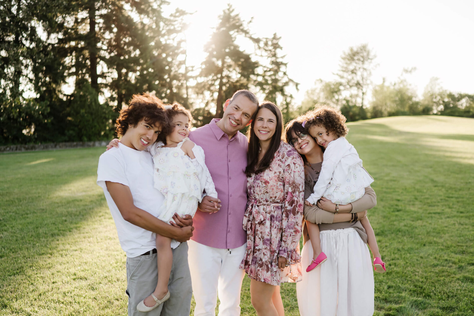 Family of six laughing and hugging on a grassy field at sunset in Heritage Park, Kirkland, WA.