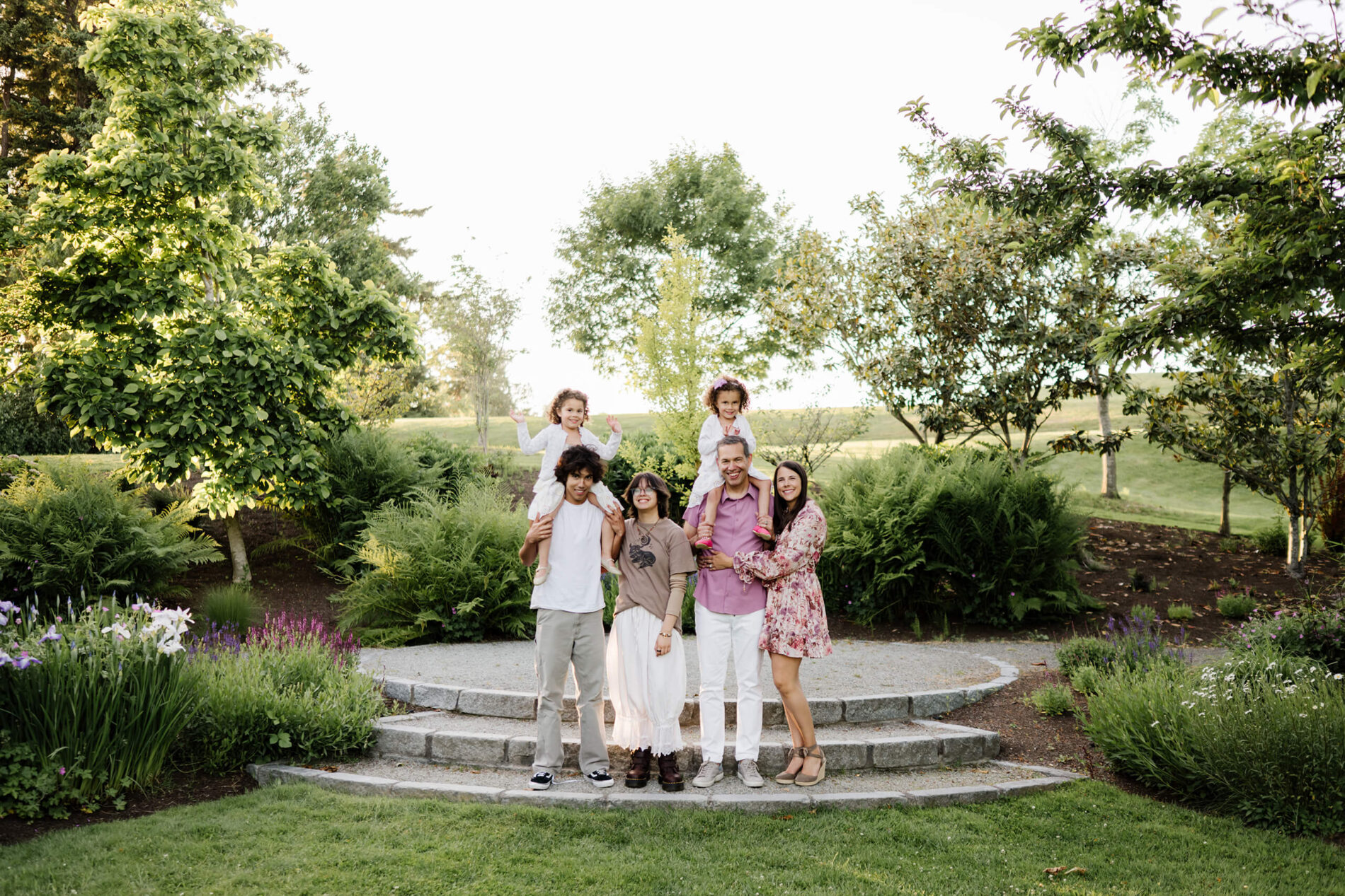 Wide view of a family standing on stone garden steps surrounded by lush ferns and flowering trees at Heritage Park, Kirkland