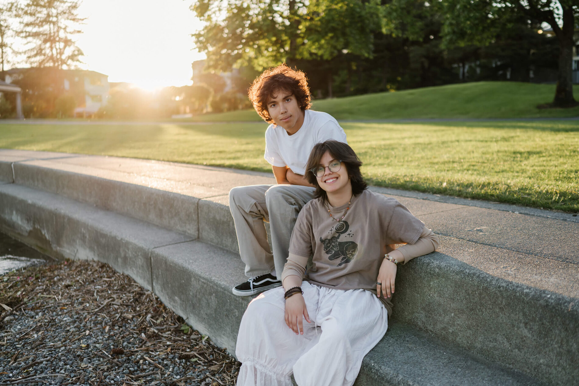 Teen brother and sister relax on concrete waterfront steps at sunset in Marina Park, Kirkland, Washington.