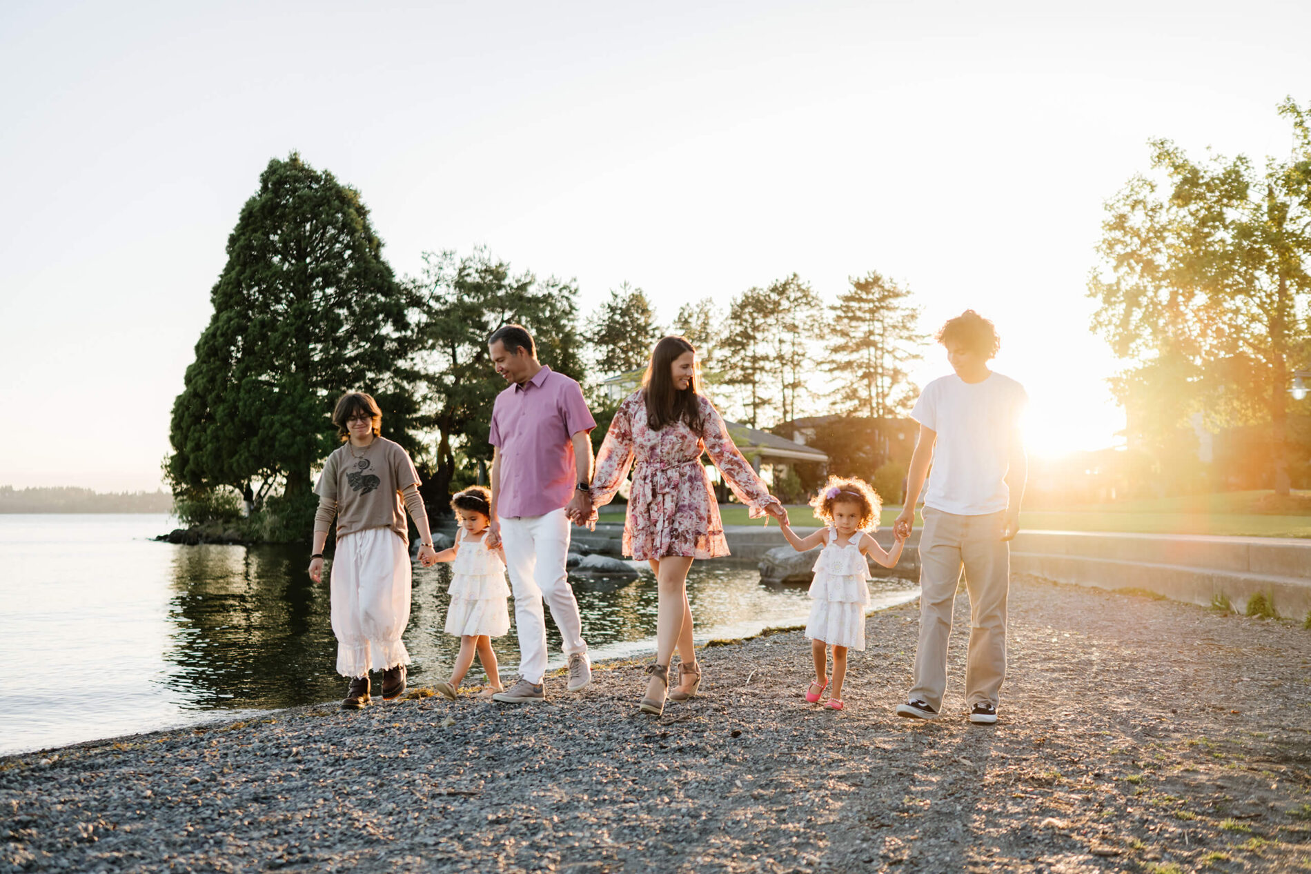 Family of six holding hands and strolling along the pebble shoreline at sunset in Marina Park, Kirkland, WA.