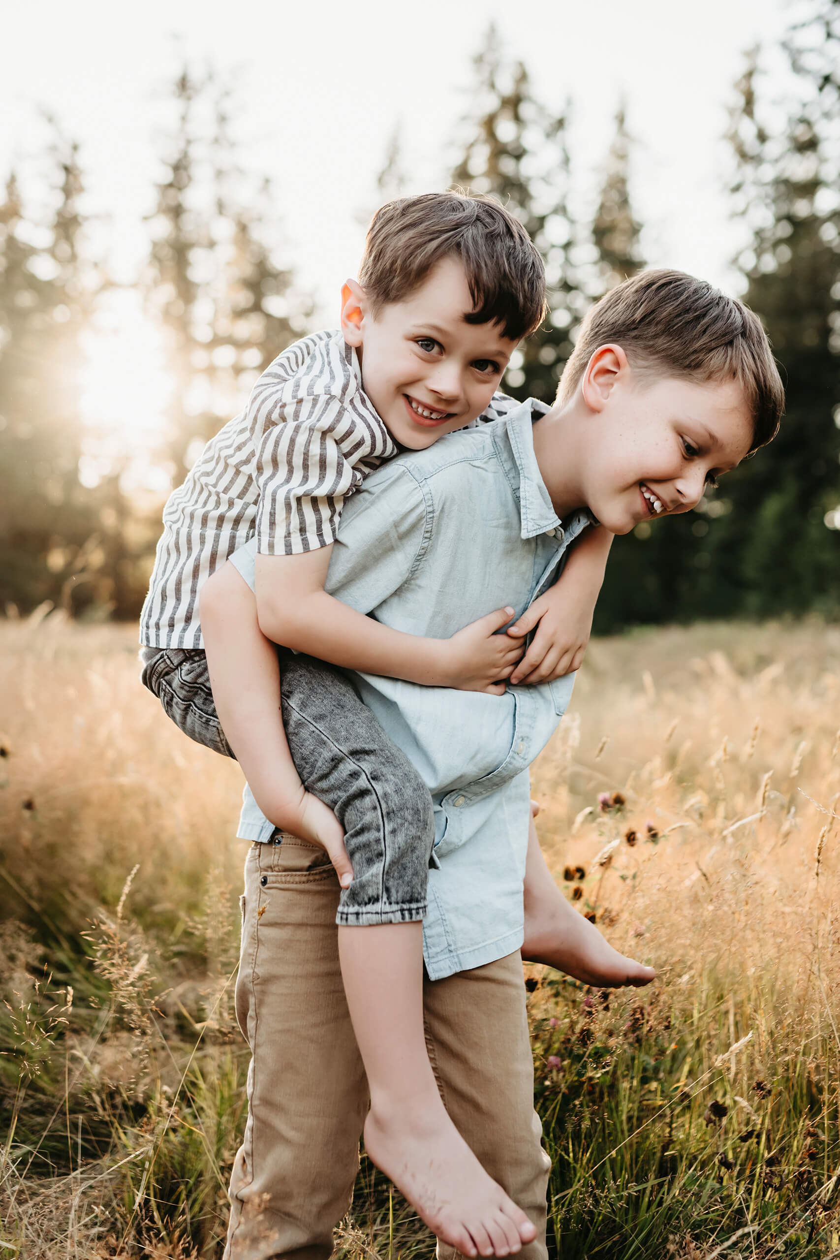 Close-up of two brothers during a playful piggyback, younger sibling smiling over older brother’s shoulder in tall grass.