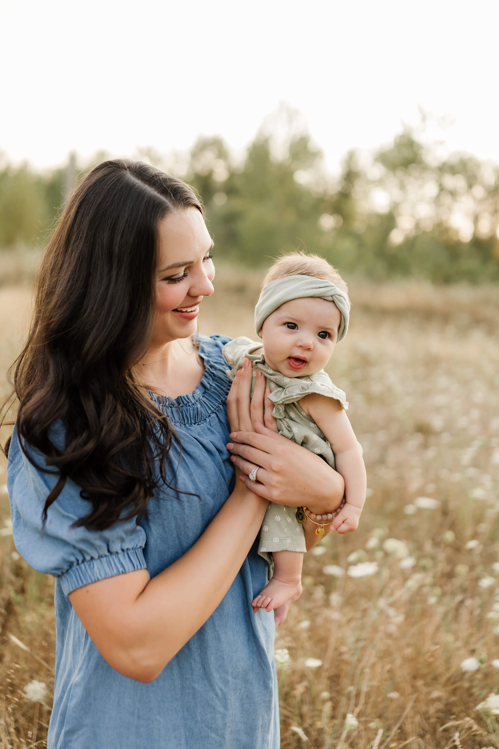 Mom cradling baby girl and smiling in a wildflower field.