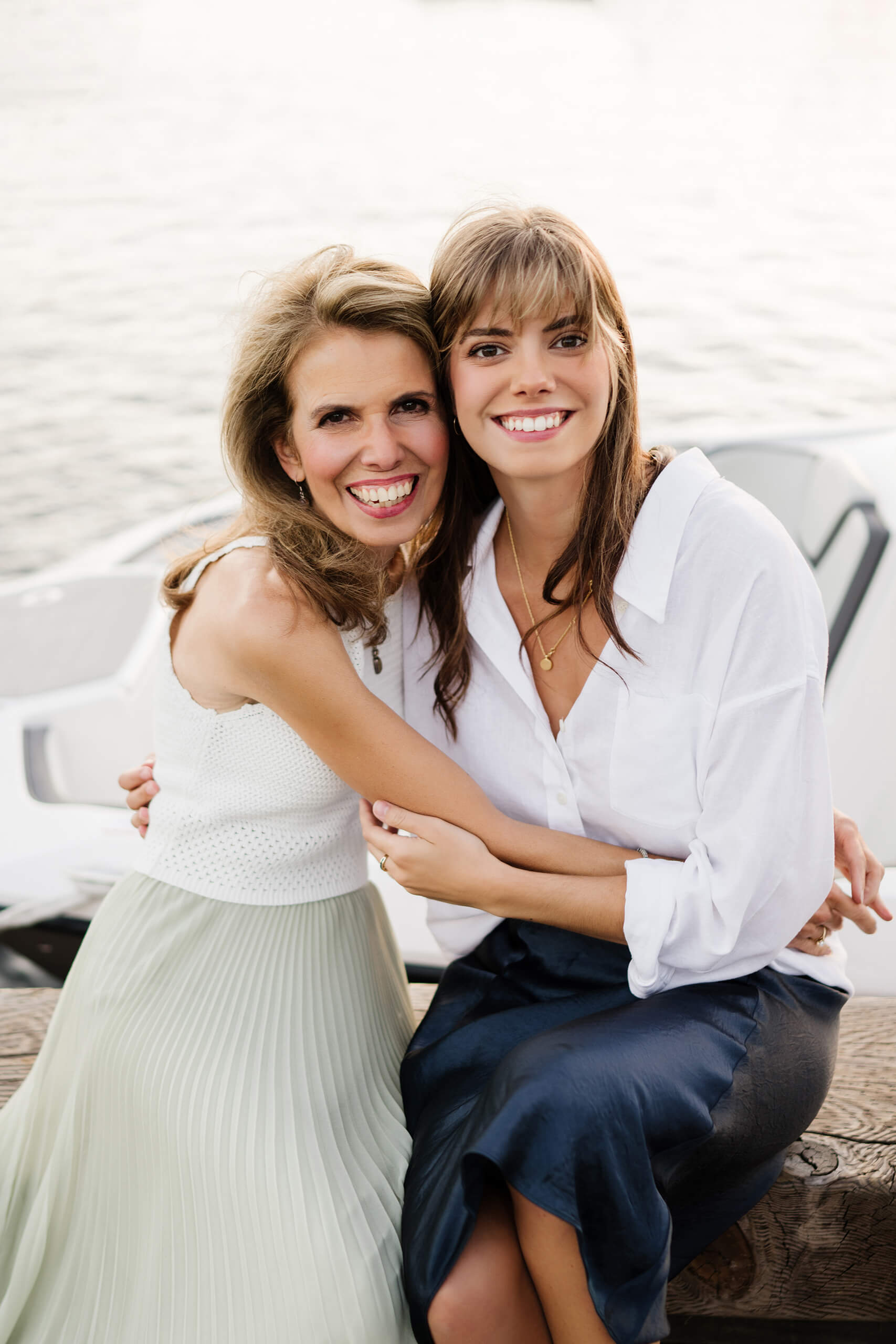 Mother and adult daughter hugging and laughing on a dock bench beside moored boat during a Carillon Point family photo session in Kirkland WA.