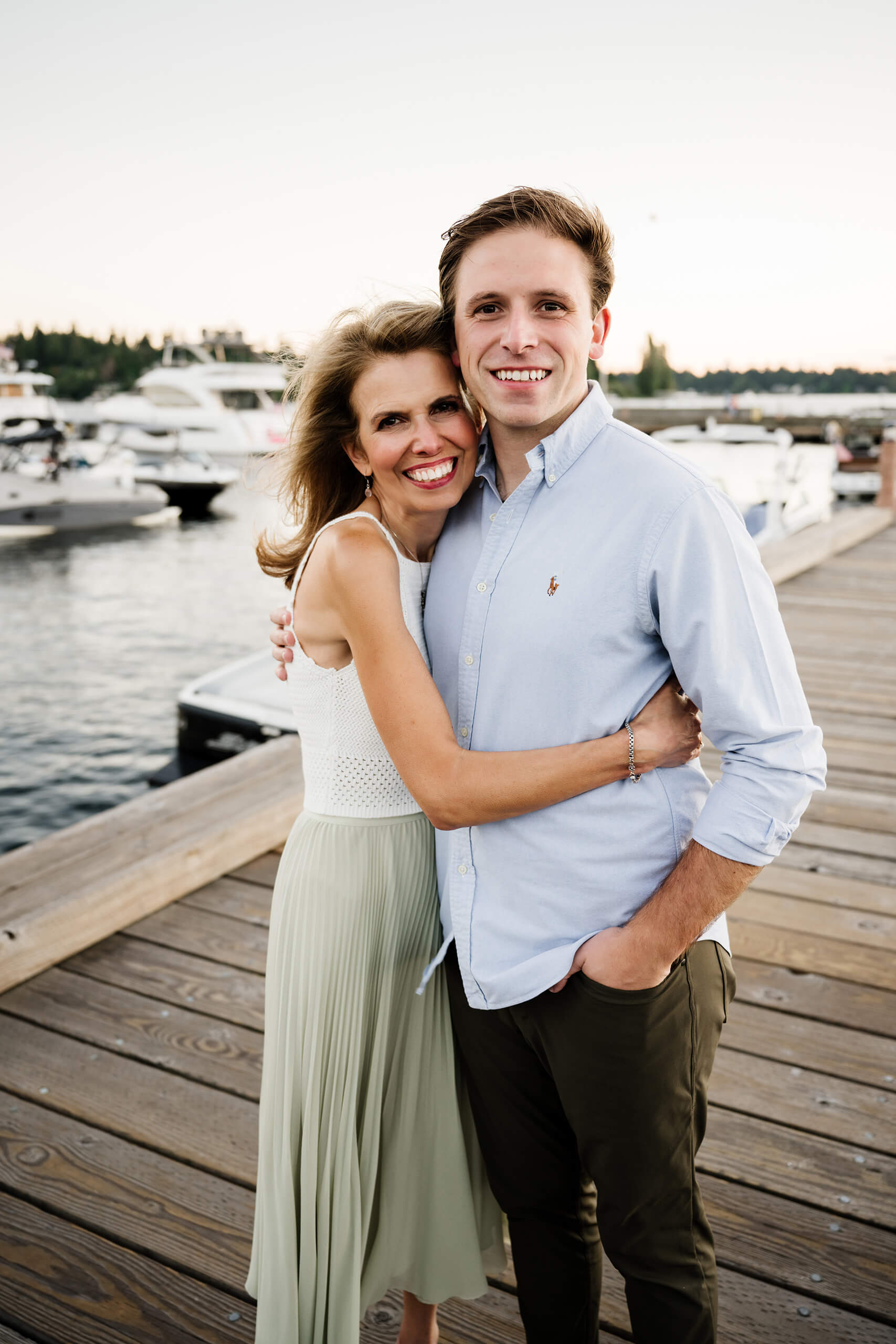 Mother embracing adult son on the Carillon Point boardwalk, yachts and pastel summer sky over Lake Washington in Kirkland WA.