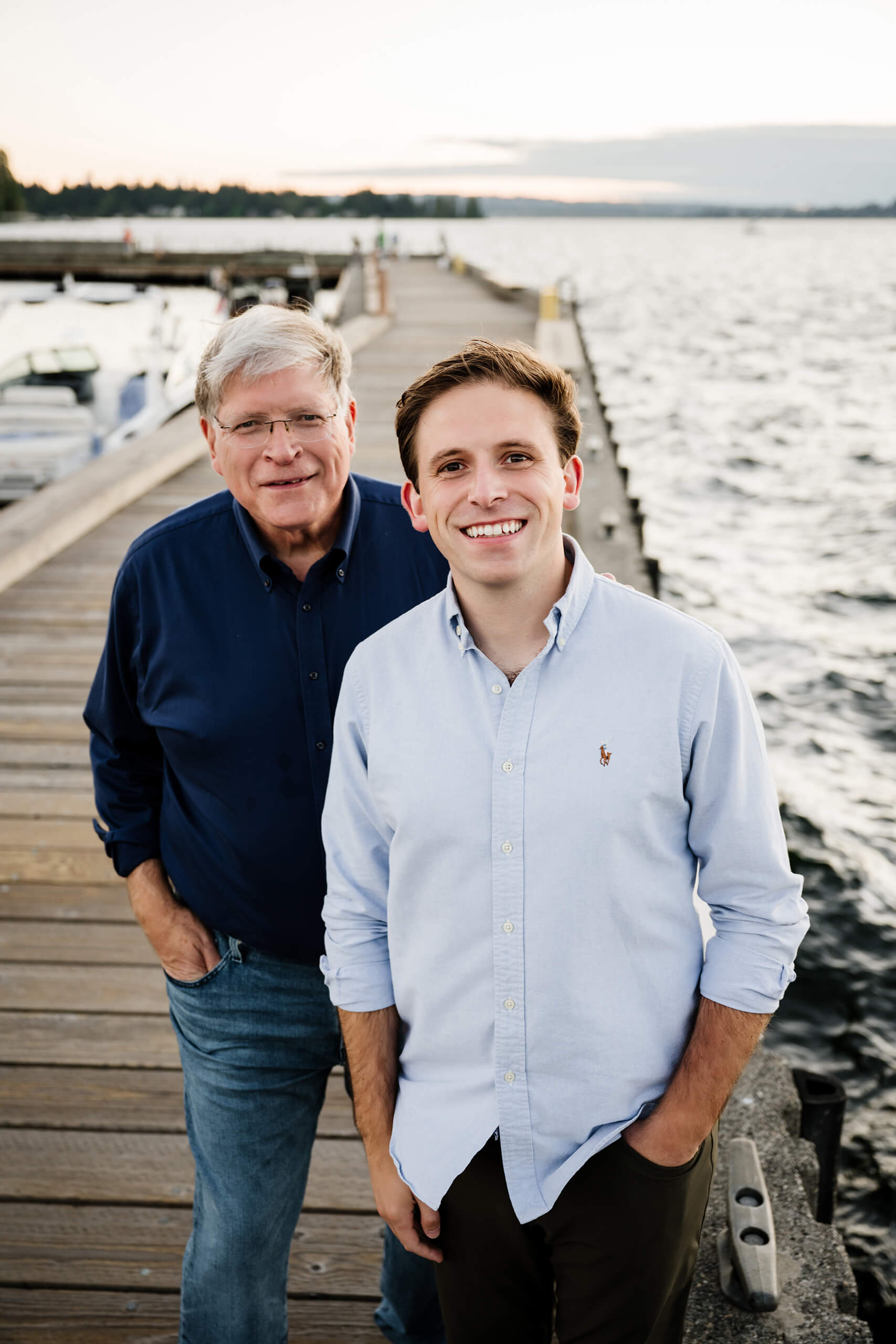 Father and adult son standing on lakeside pier, wooden planks leading out over Lake Washington at Carillon Point, Kirkland WA.
