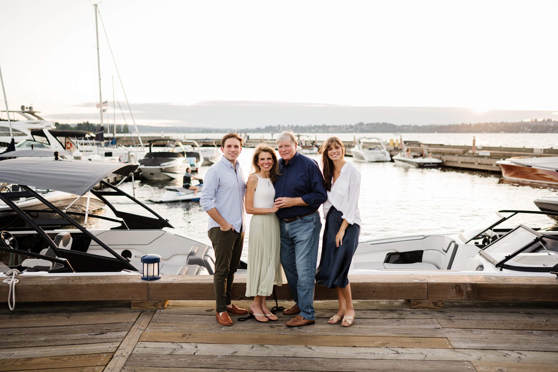 Sunset portrait of family standing together along the marina edge, gleaming boats and golden light over Lake Washington at Carillon Point, Kirkland WA.