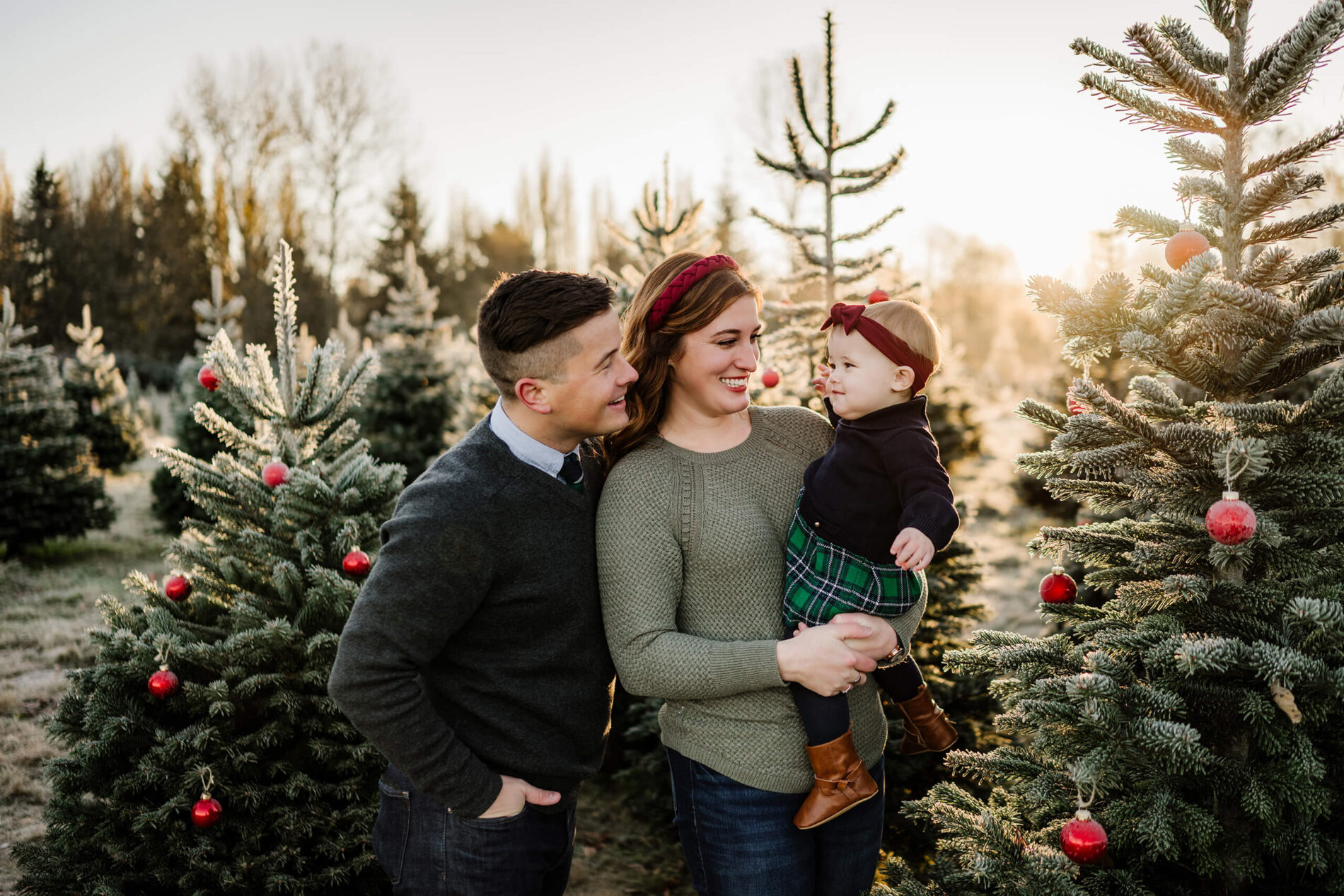 Family smiling with toddler – Seattle Christmas tree farm holiday mini session with decorated evergreens.