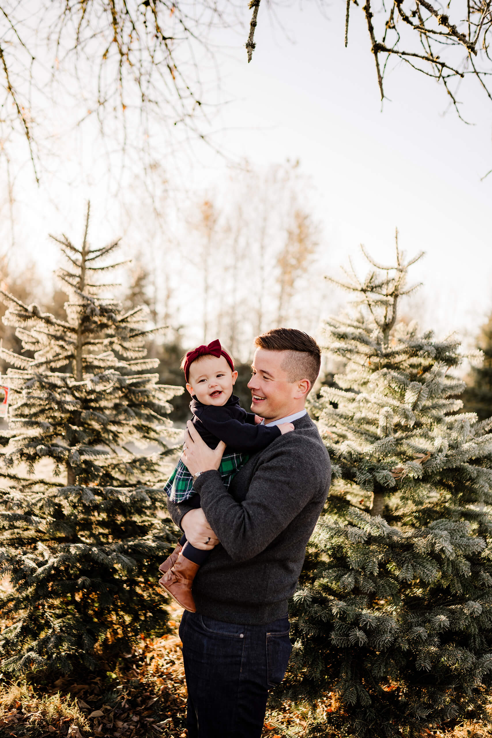 Father holding baby girl – Seattle Christmas tree farm holiday photo of dad lifting daughter at golden hour.