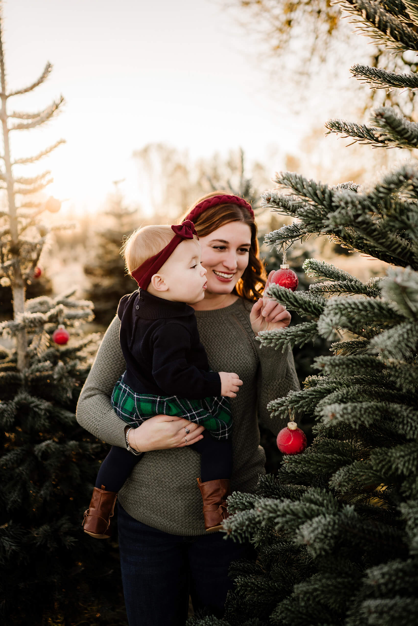 Mother decorating with toddler – Seattle holiday portraits of mom and daughter looking at ornaments on Christmas tree.