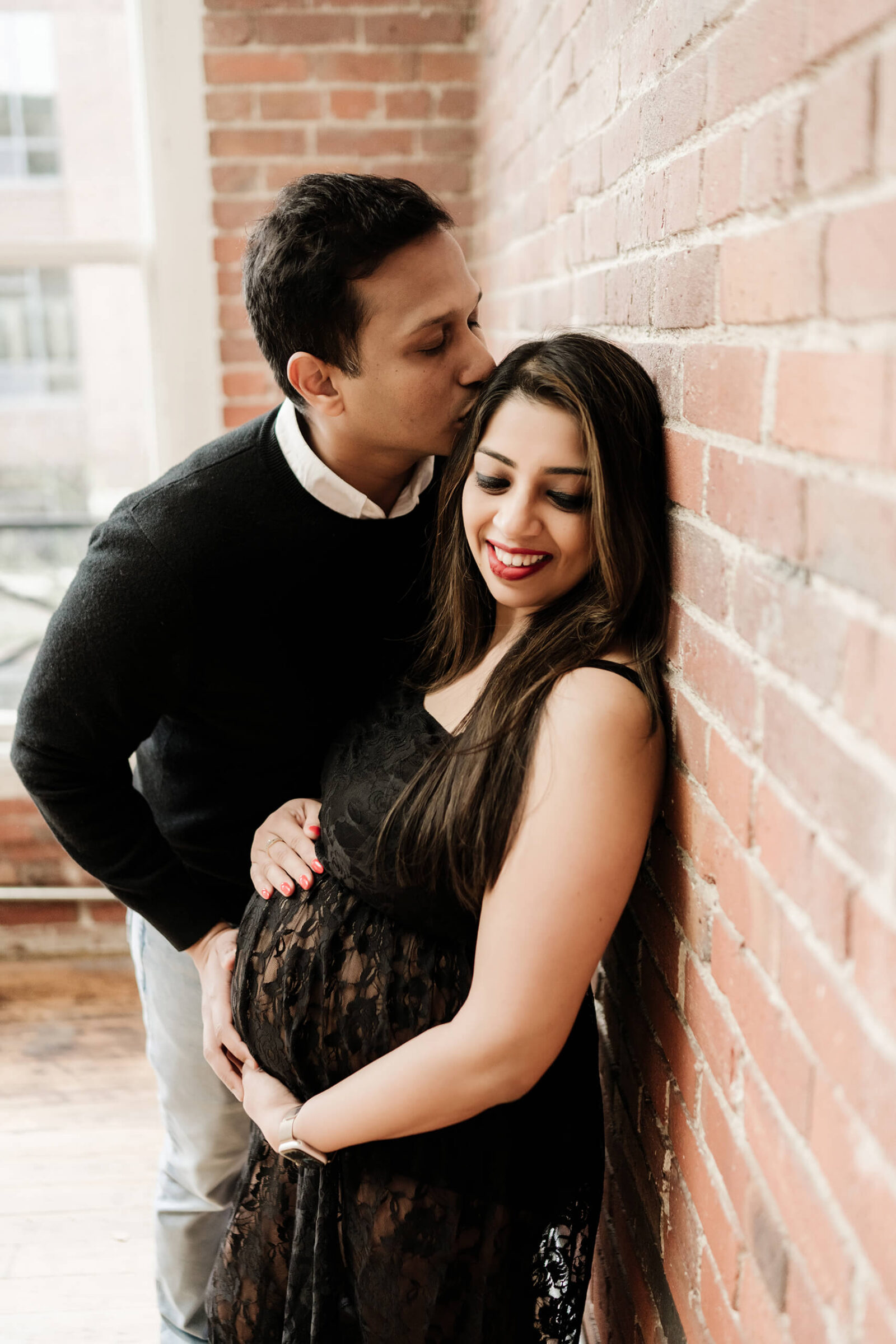Seattle maternity photography session in studio with expecting couple sharing a tender moment by a brick wall.