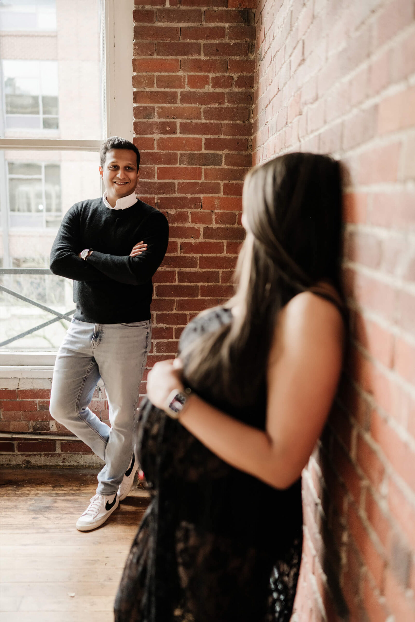 Seattle maternity photographer captures candid studio moment with expecting couple by brick wall