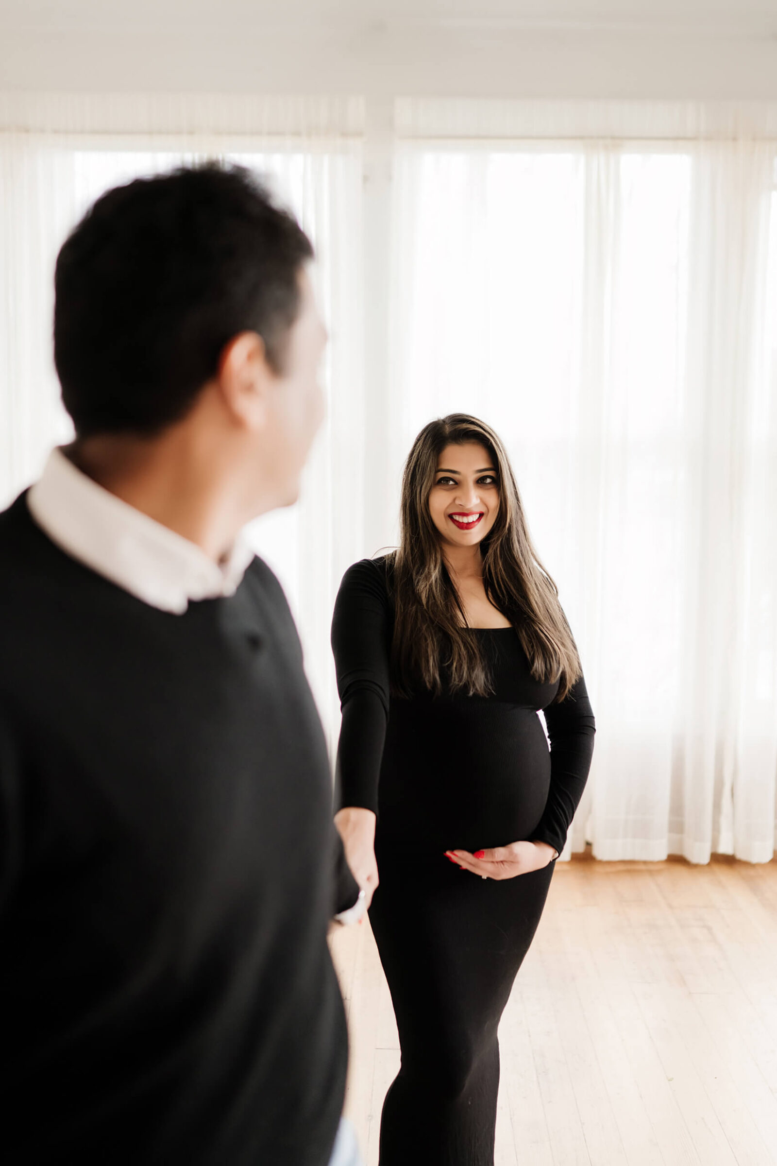 Seattle maternity photography with expectant mother in black dress holding hands with partner during studio session