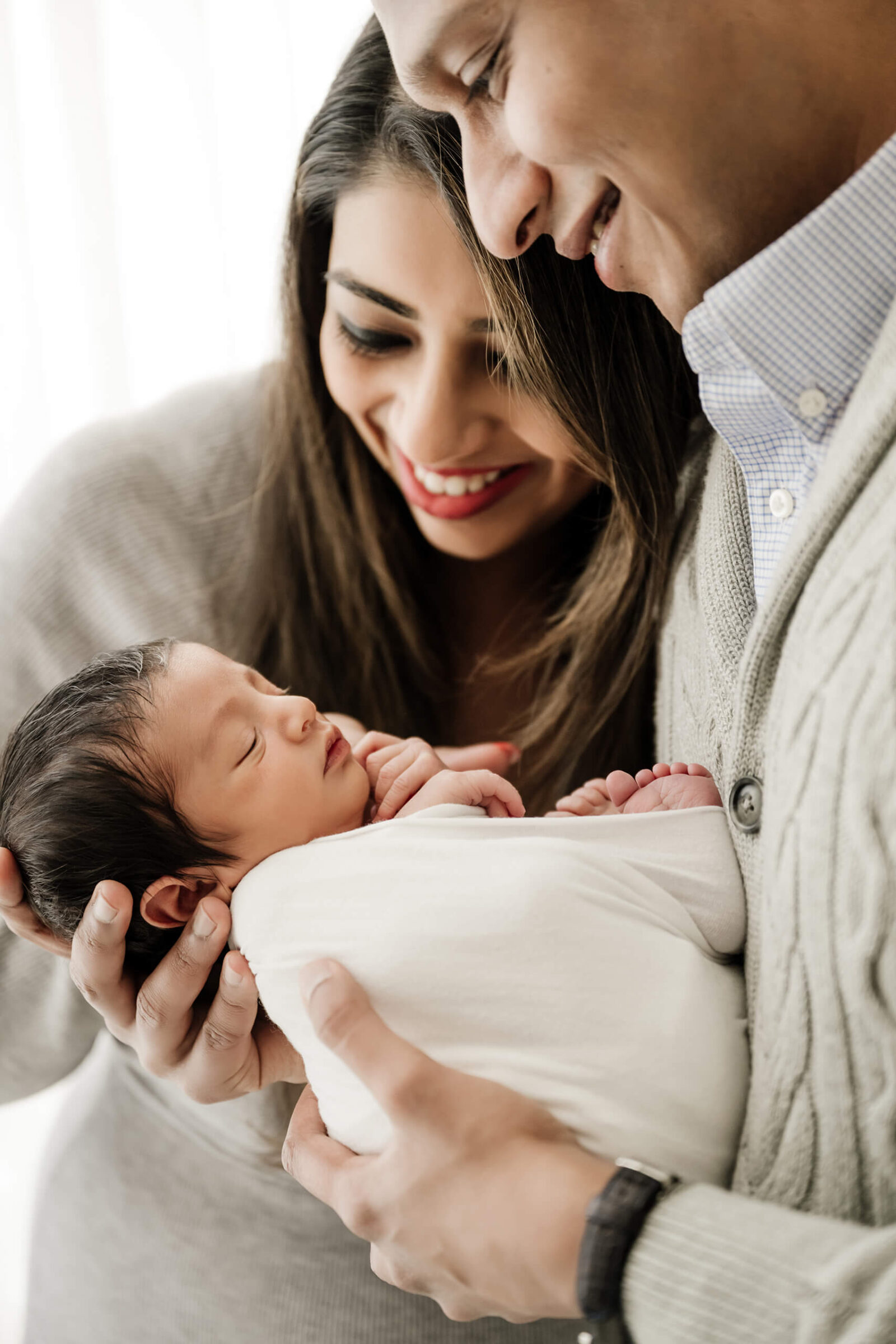 Seattle newborn photography session with parents smiling while holding their baby swaddled in white wrap.