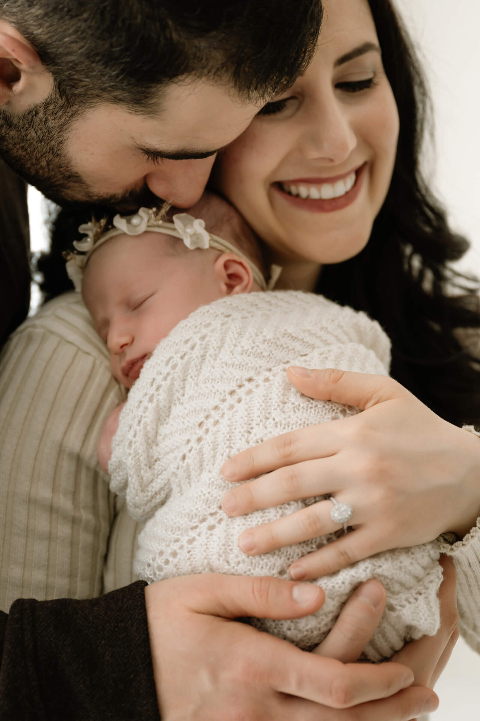 Close family moment with parents embracing their sleeping newborn baby wrapped in white knit during a Seattle newborn photography session focused on connection and warmth.