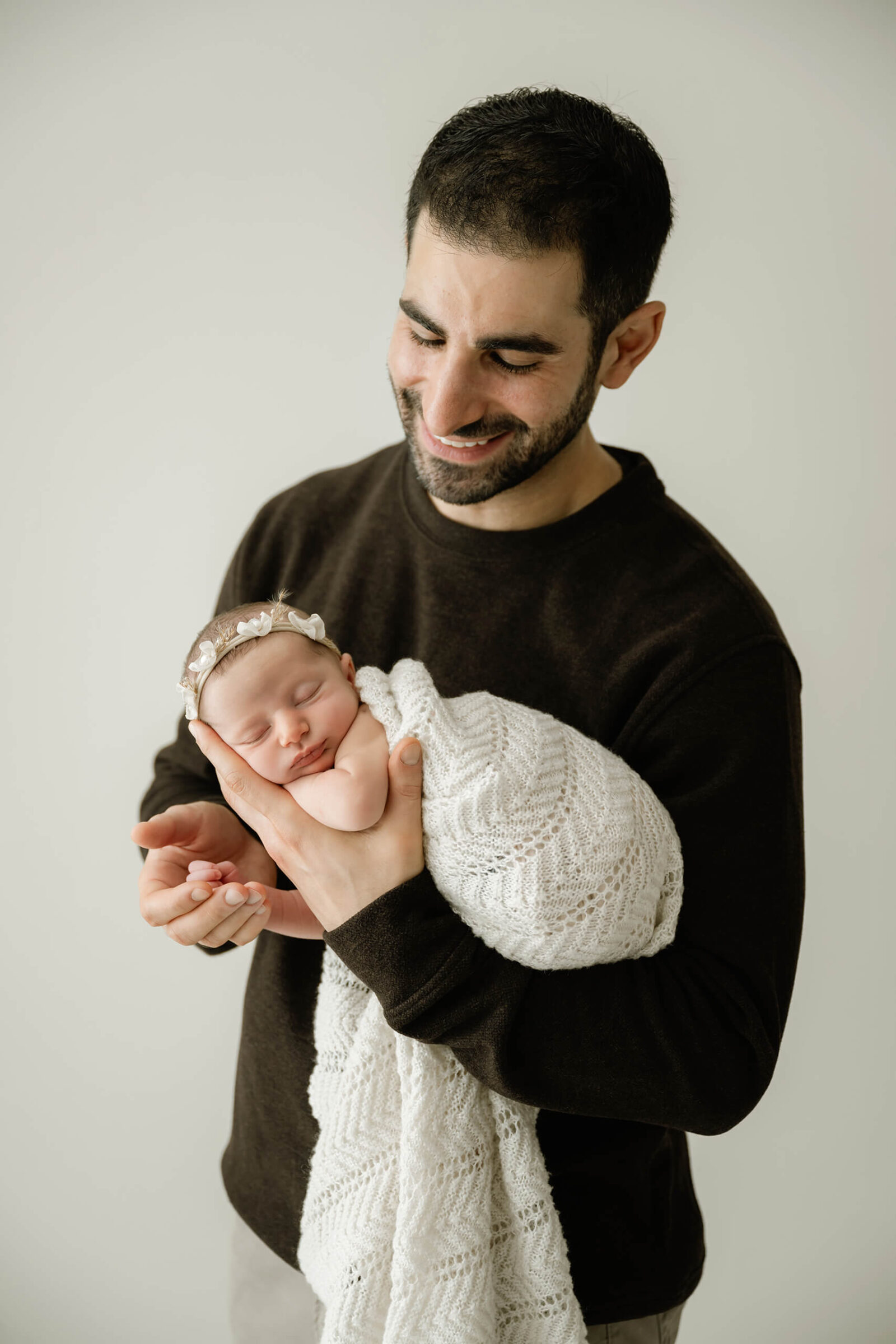 Father cradling his swaddled newborn daughter in a white textured blanket, captured in timeless natural light during a Seattle newborn studio session.