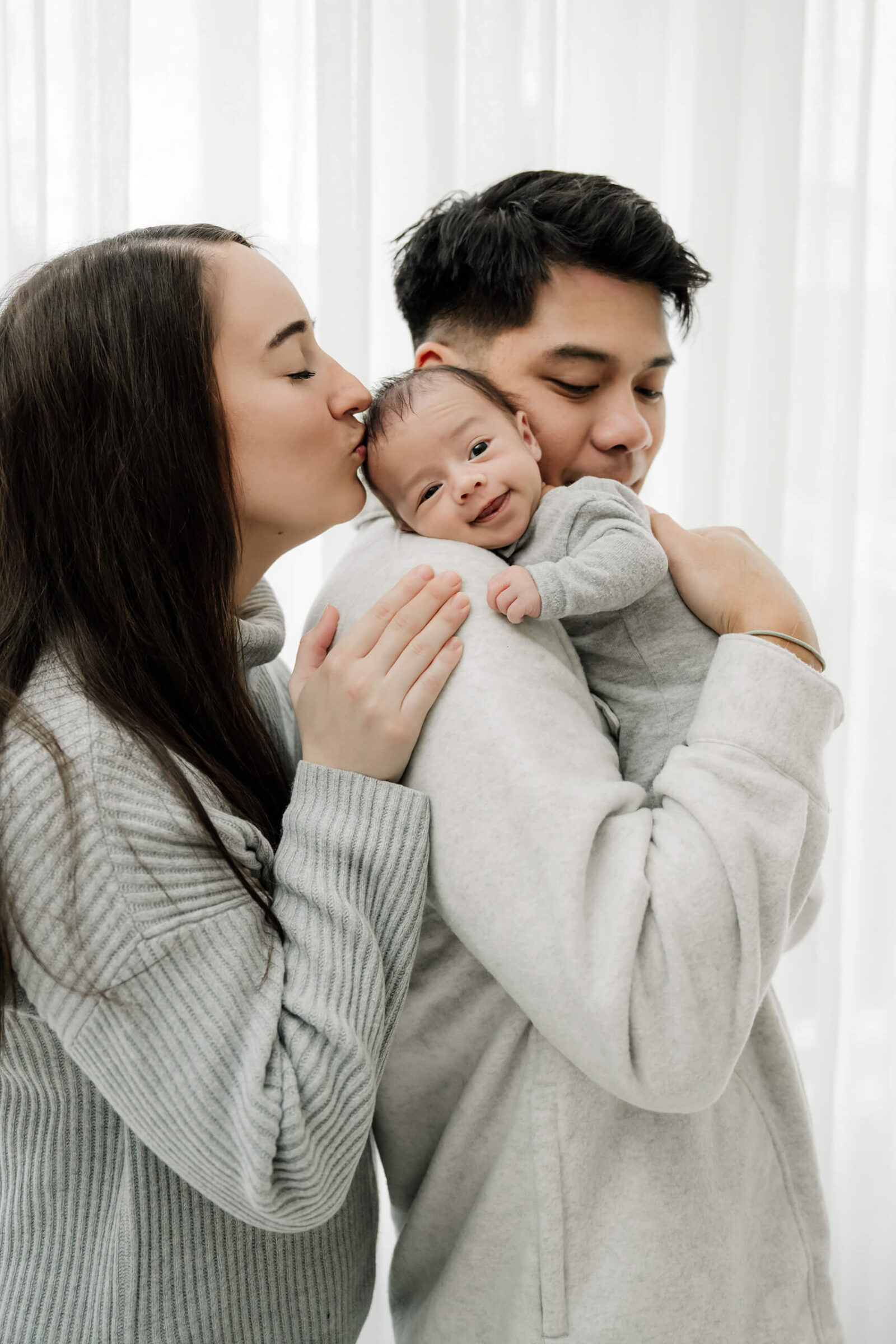 Parents snuggling their newborn baby during a soft natural-light photo session, showcasing tender connection and calm joy.
