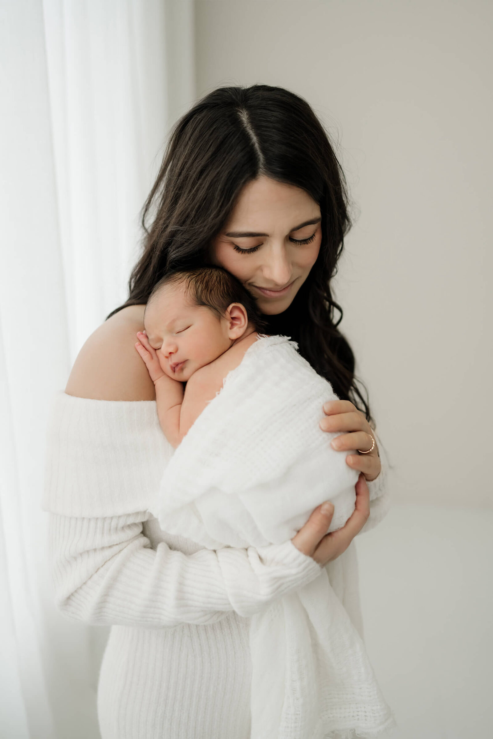 Mother holding her sleeping newborn close to her shoulder during a serene in-studio photo session.