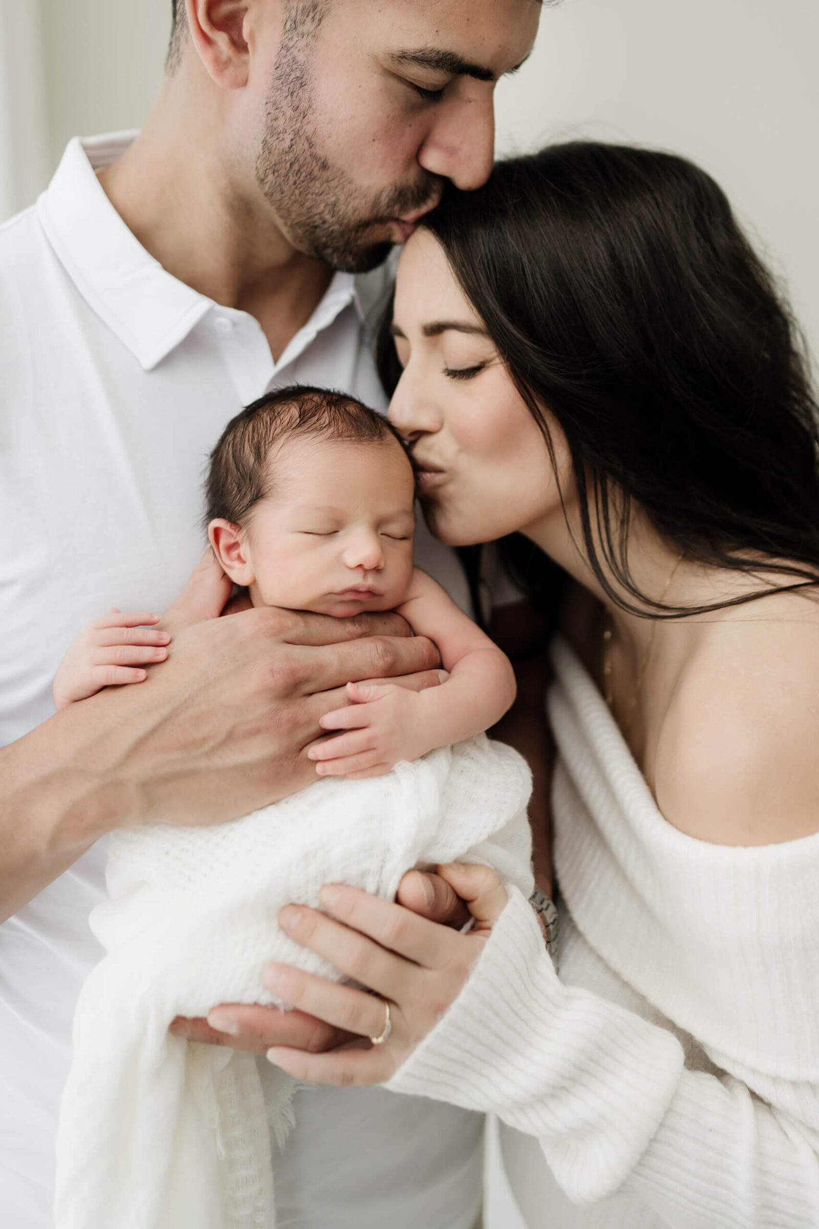 Parents kissing their sleeping newborn during a calm, connection-focused newborn photoshoot.