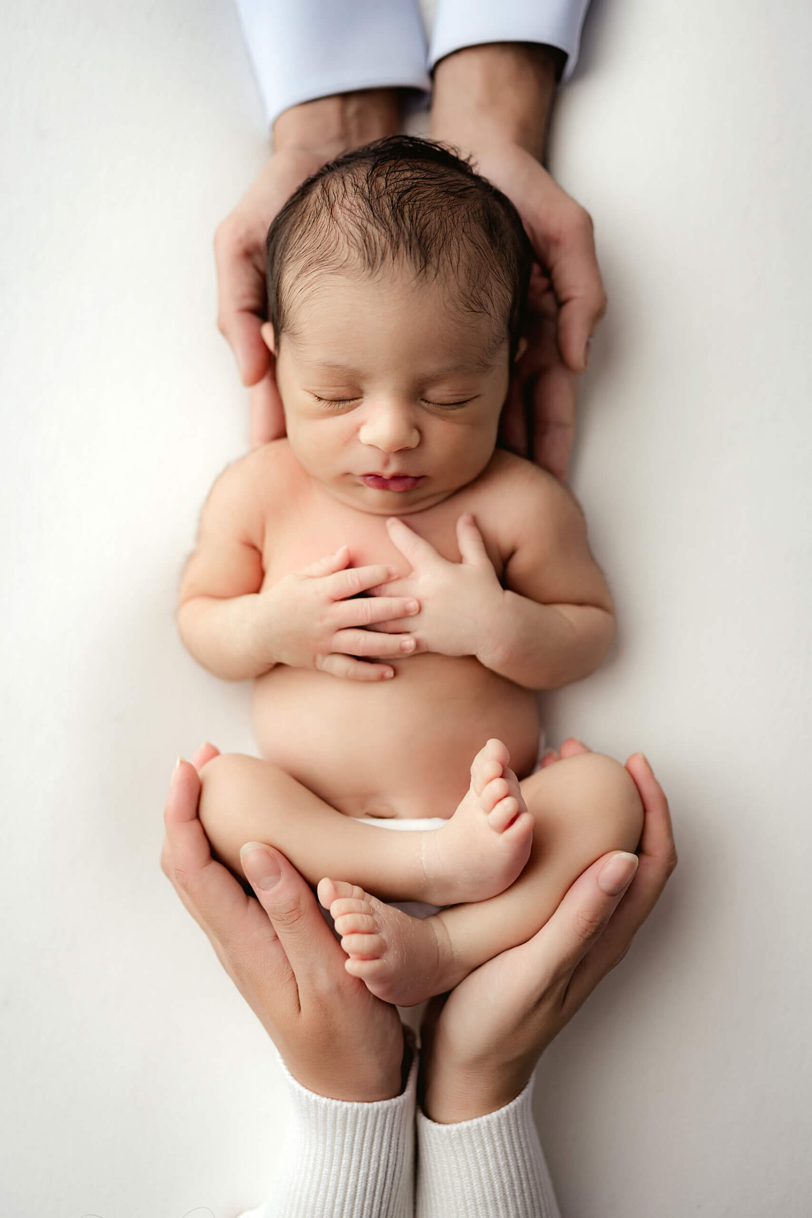 Newborn baby sleeping in parents’ hands during a minimal, light-filled studio newborn photoshoot in Seattle.