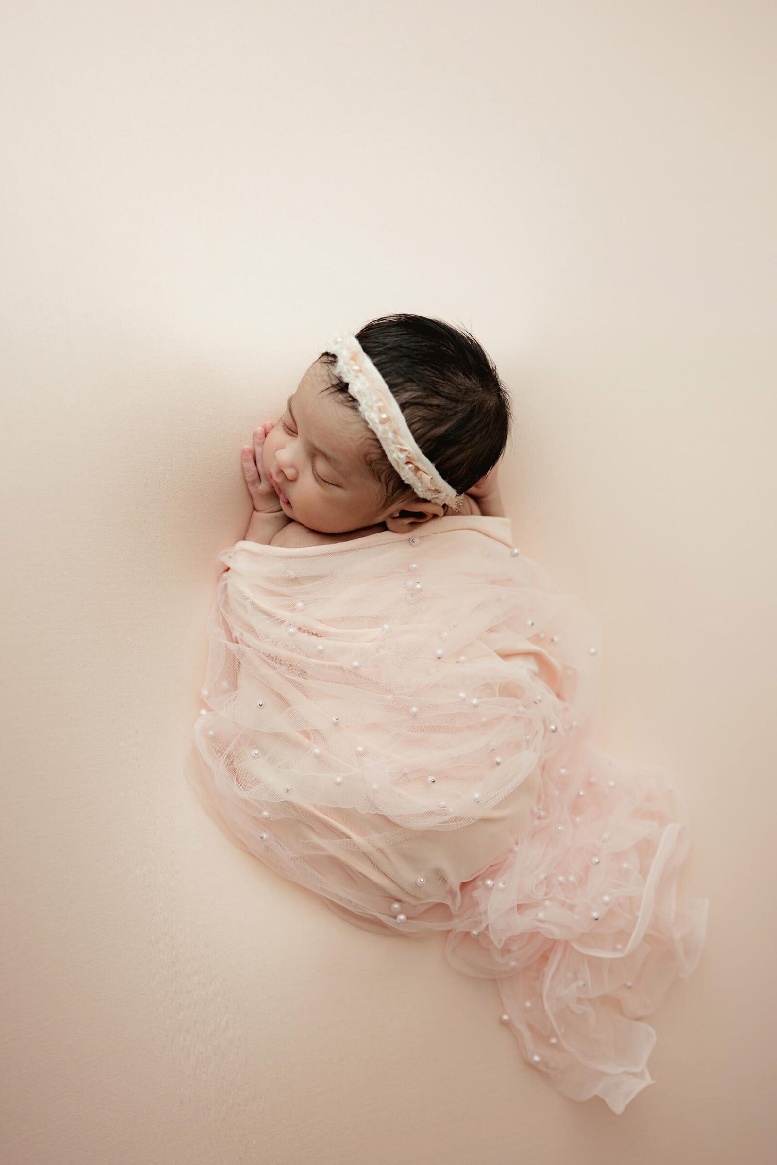 Newborn baby girl sleeping peacefully in a pearl-adorned pink wrap during a soft, timeless Seattle newborn photoshoot.
