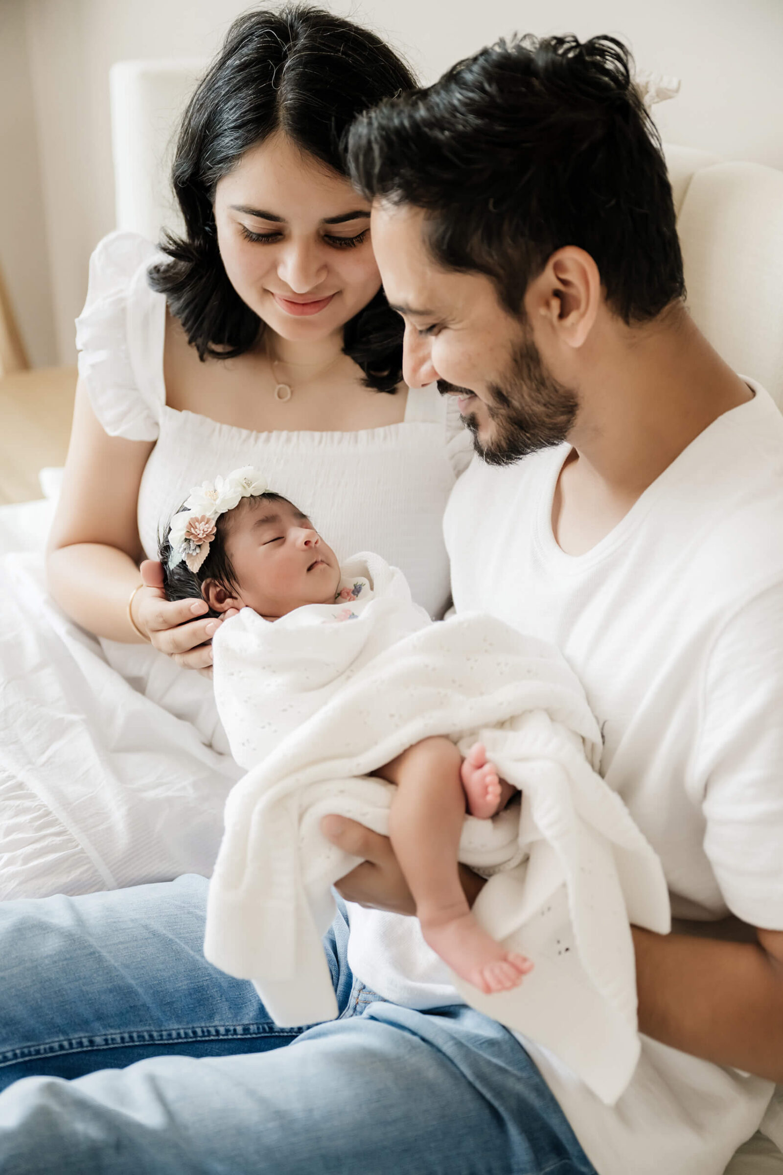 Parents smiling down at their newborn baby girl wrapped in a white blanket during a natural in-home newborn photoshoot in Seattle.