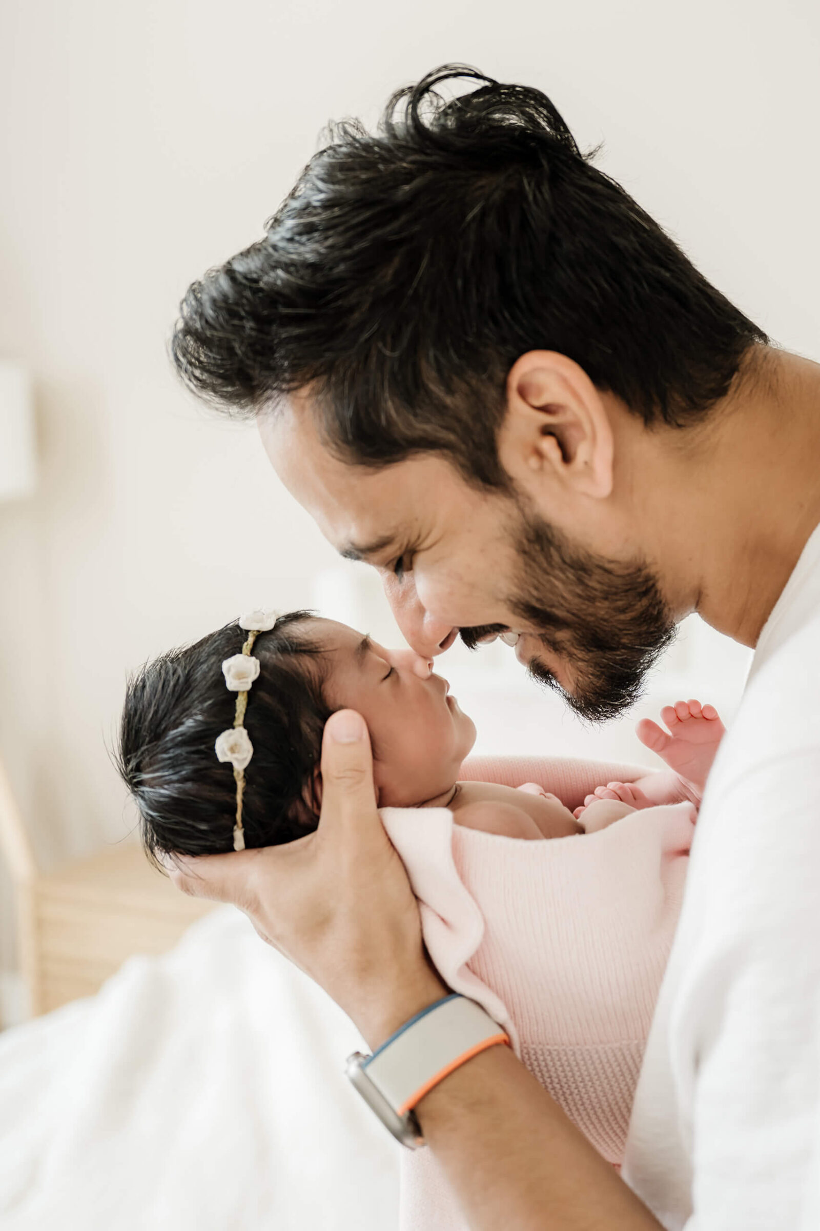 Father touching noses with his newborn daughter wrapped in a pink blanket during a warm, connection-filled in-home newborn photo session.