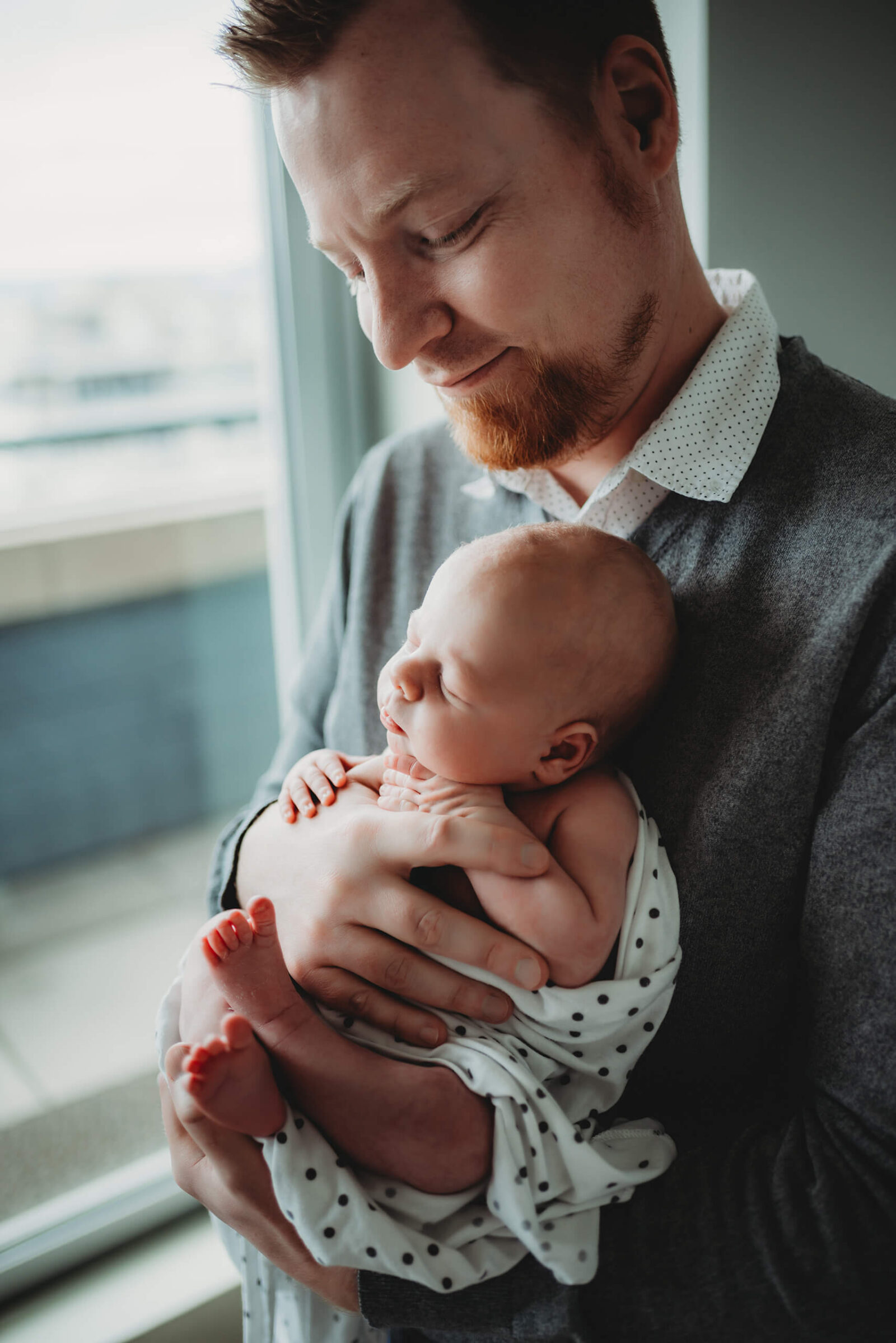 Father holding his newborn baby in a cozy nursery during a documentary-style in-home newborn photo session.